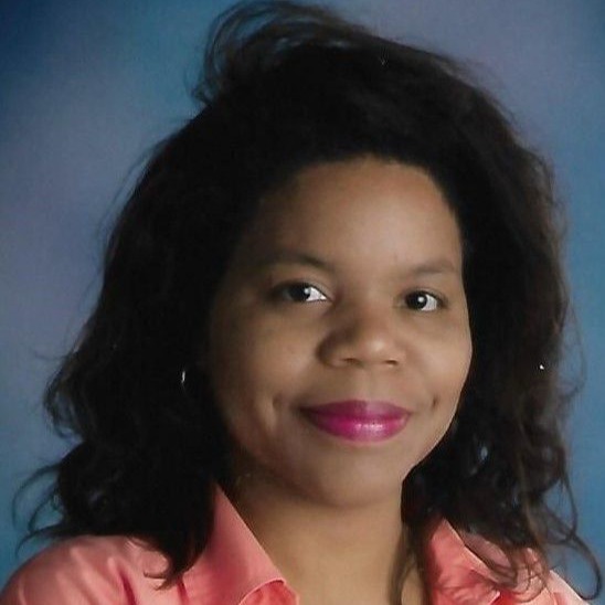 The portrait shows Ms. McFarland with dark, shoulder-length wavy hair against a classic mottled blue studio background. She is wearing a light peach or coral button-down shirt unbuttoned over a plain white top, and is lightly smiling with bright pink lipstick.