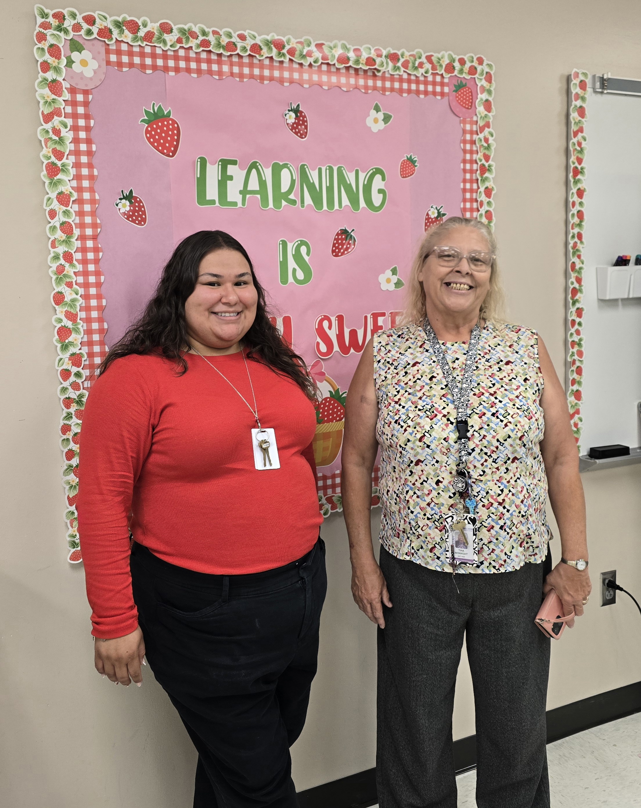 Ms. Hernandez and Ms. McKnight stand in front of the bulletin board in the Technology 2 classroom