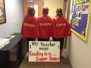 First grade teachers standing facing away from the camera with a sign that reads my teacher says reading is a superpower