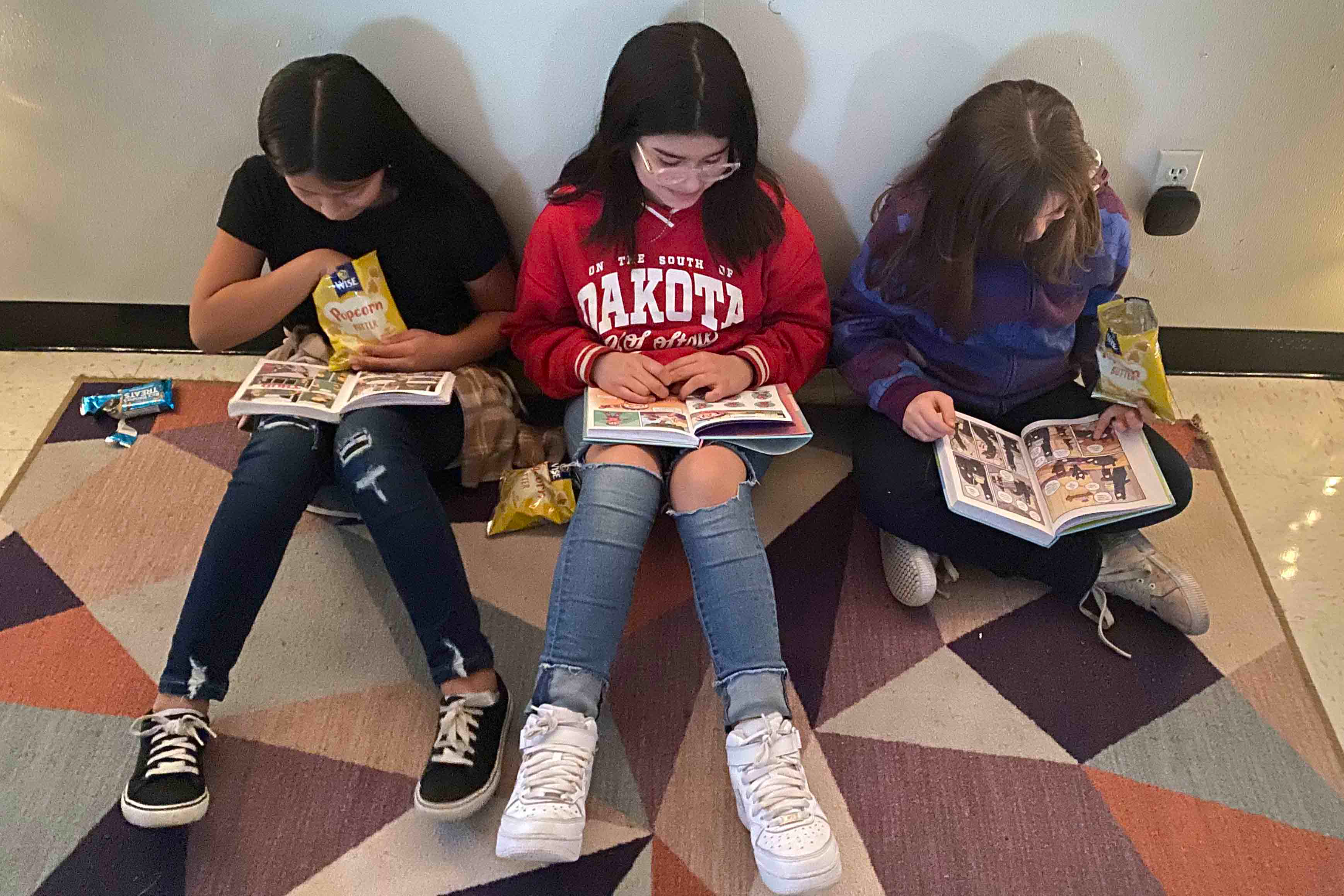 Three students are sitting on the floor and reading books