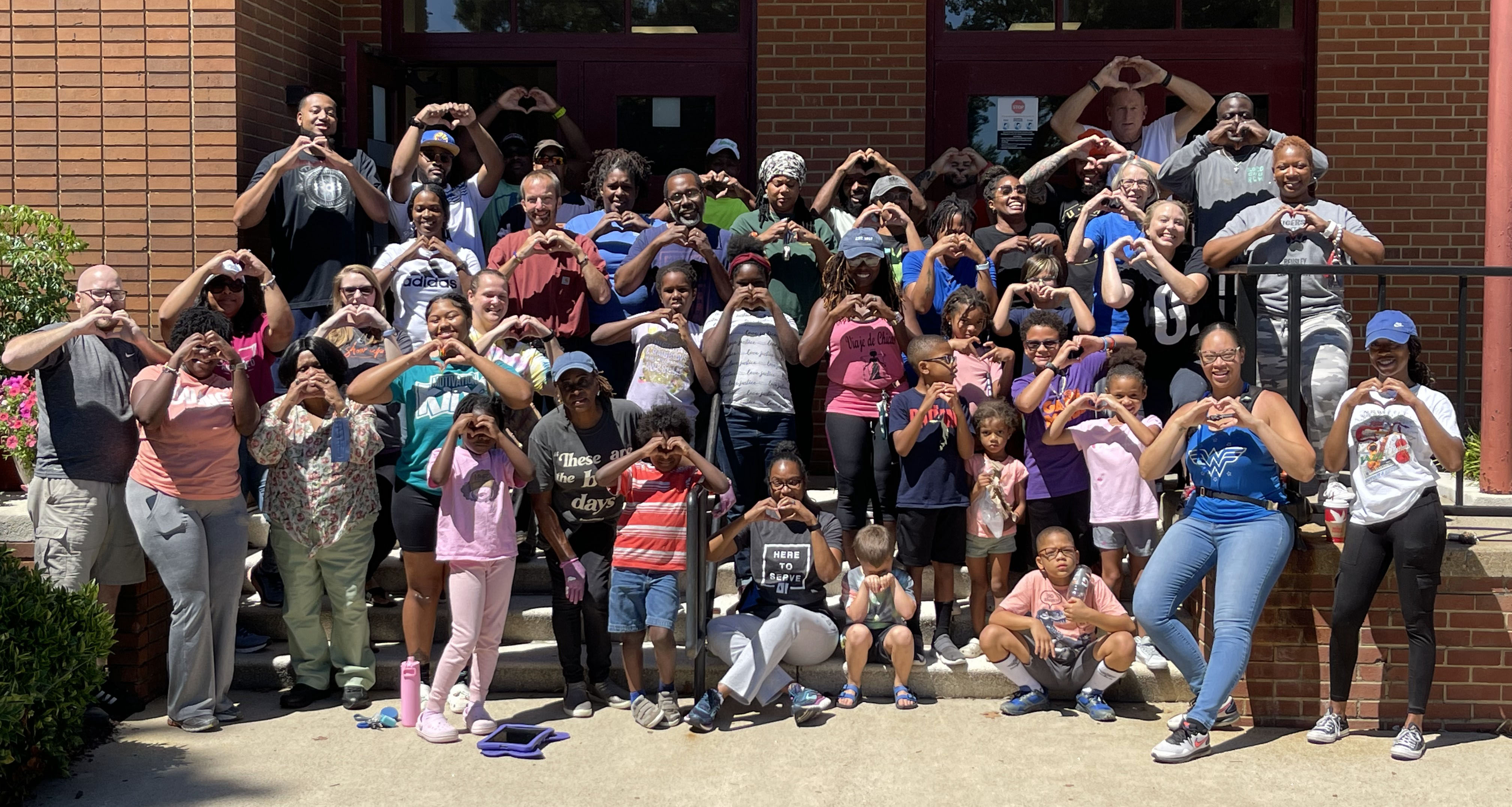 A large group of staff and students making a heart sign with their hands