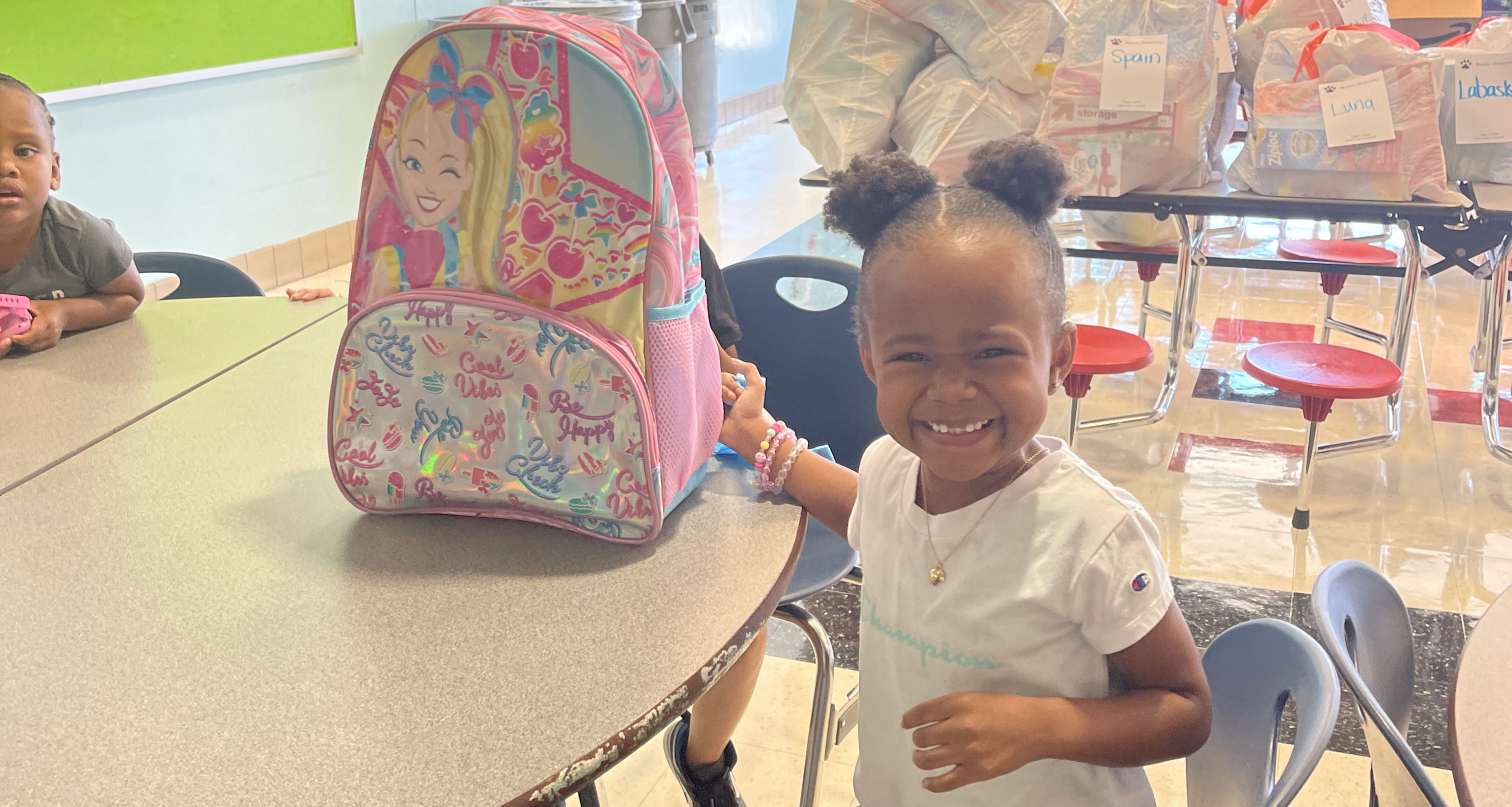 A student smiling in the cafeteria with her backpack next to her