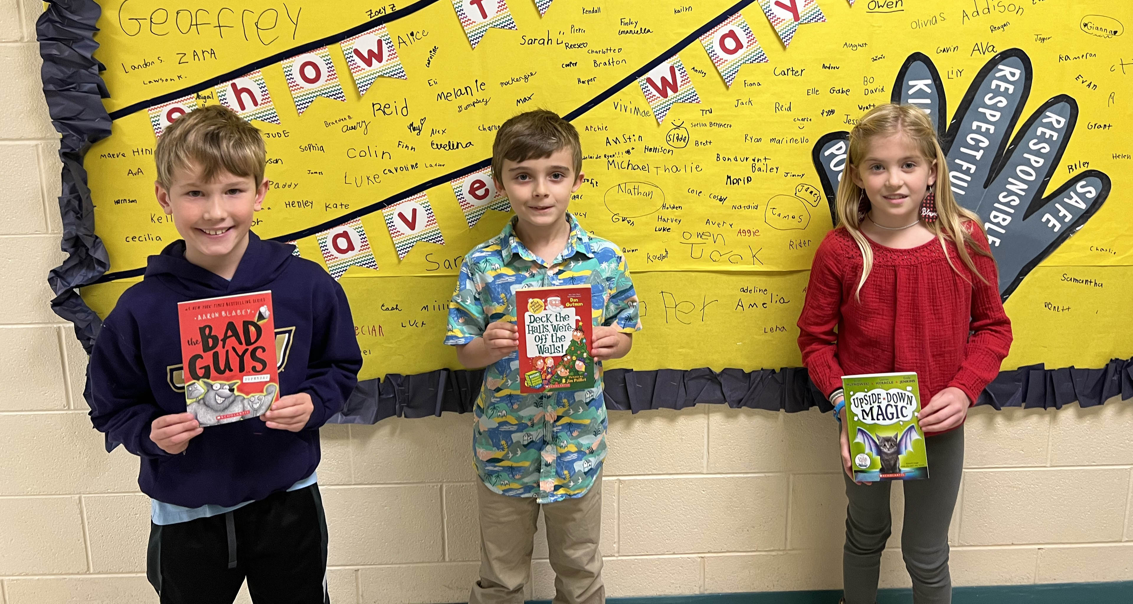 Three students hold up their books for the camera.