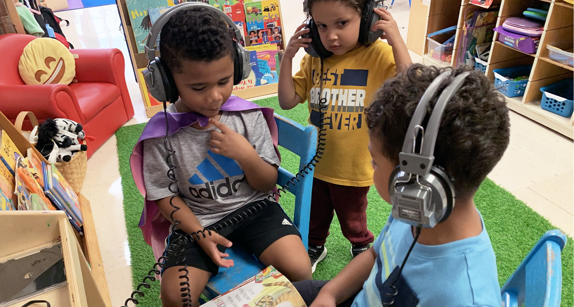 Three students wearing headphones and following along with a book