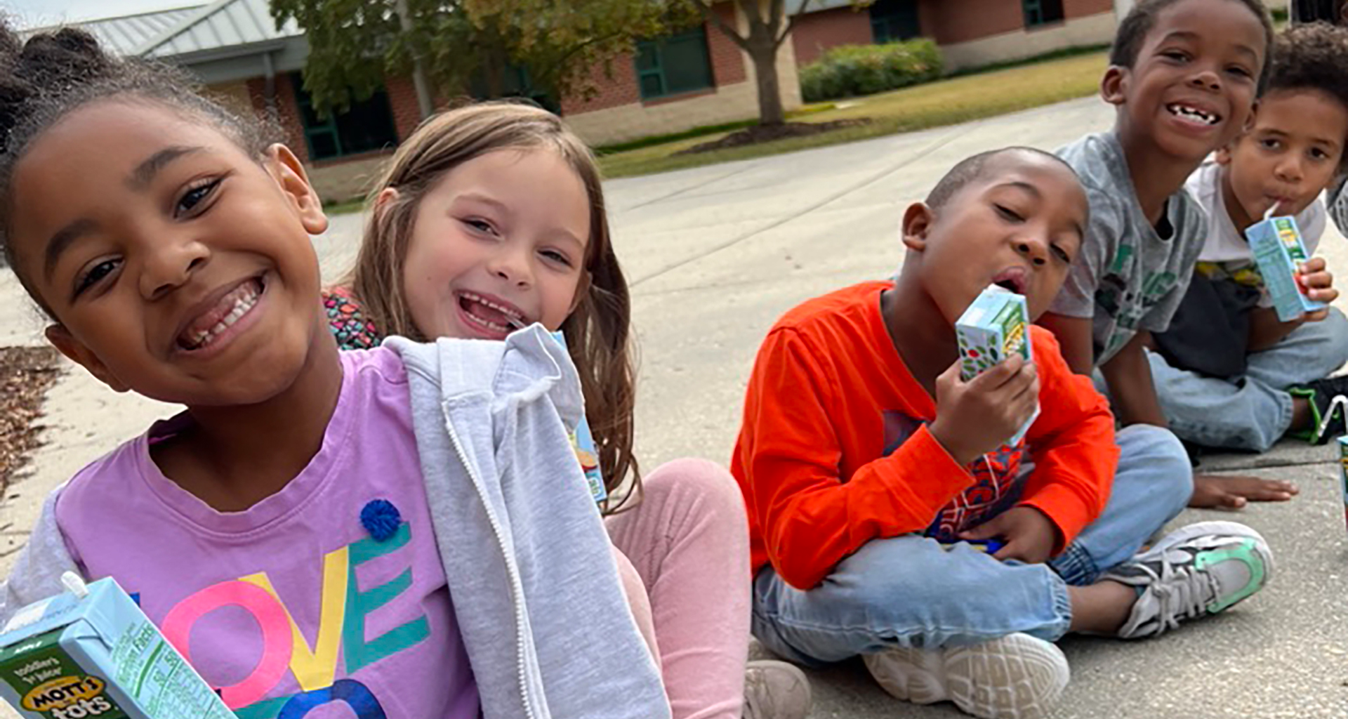 Children drinking juice boxes outside on the sidewalk