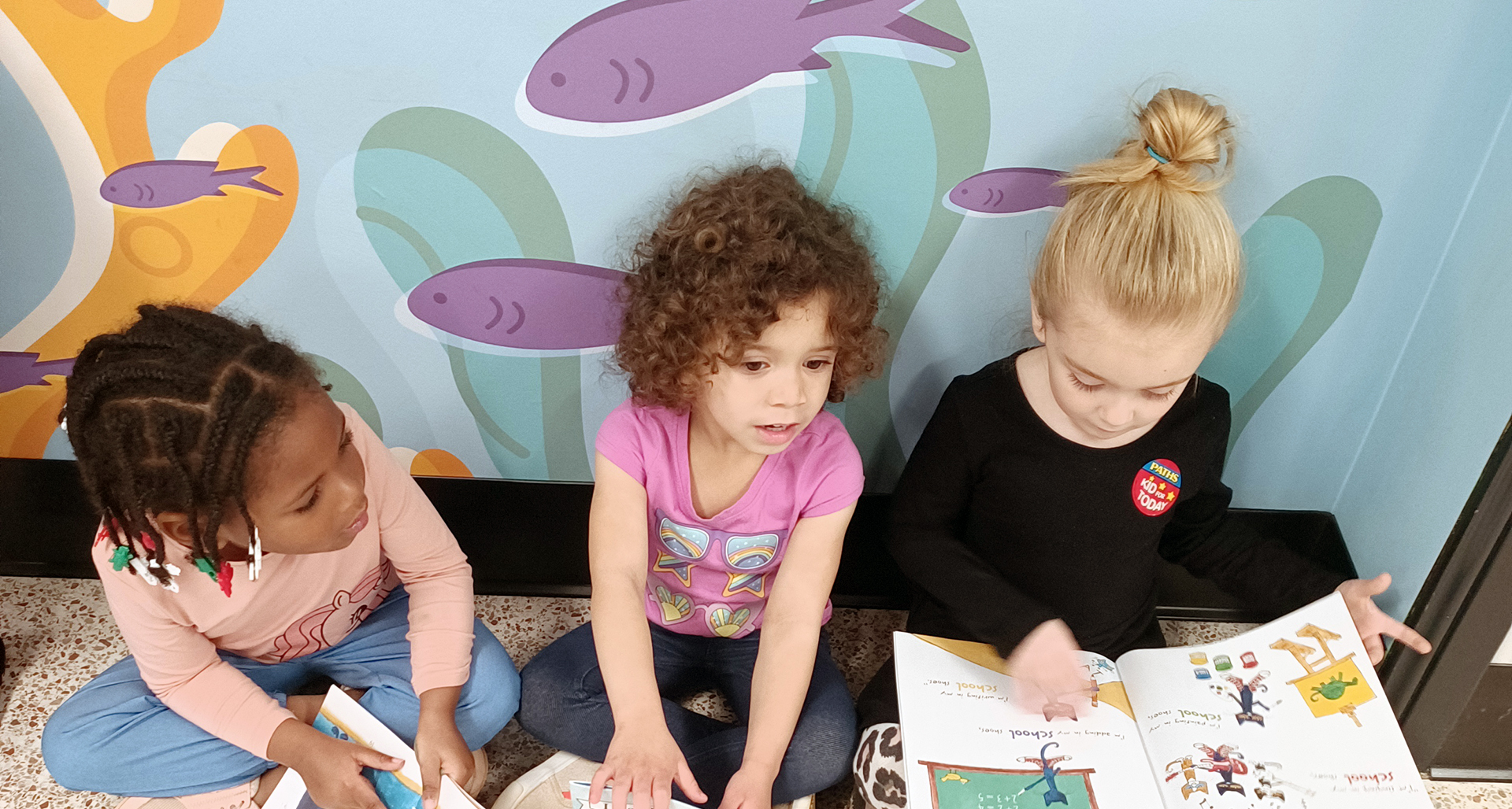 Three young girls sitting on the floor reading together.