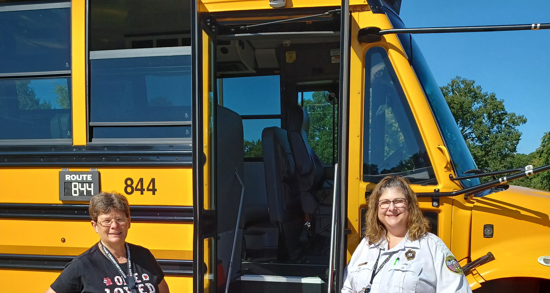 Two bus drivers pose in front of bus.