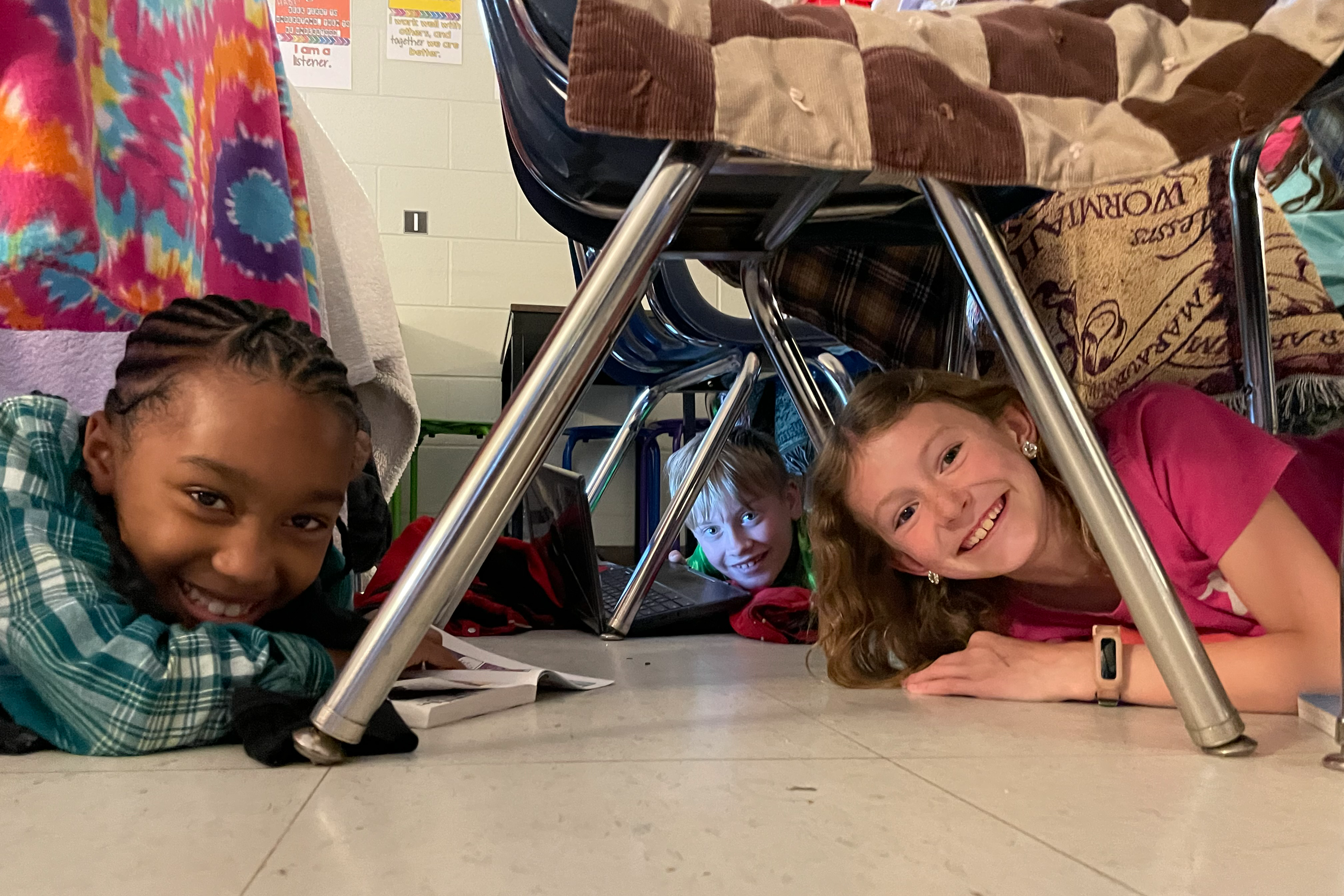 Three students under a fort made of chairs and blankets