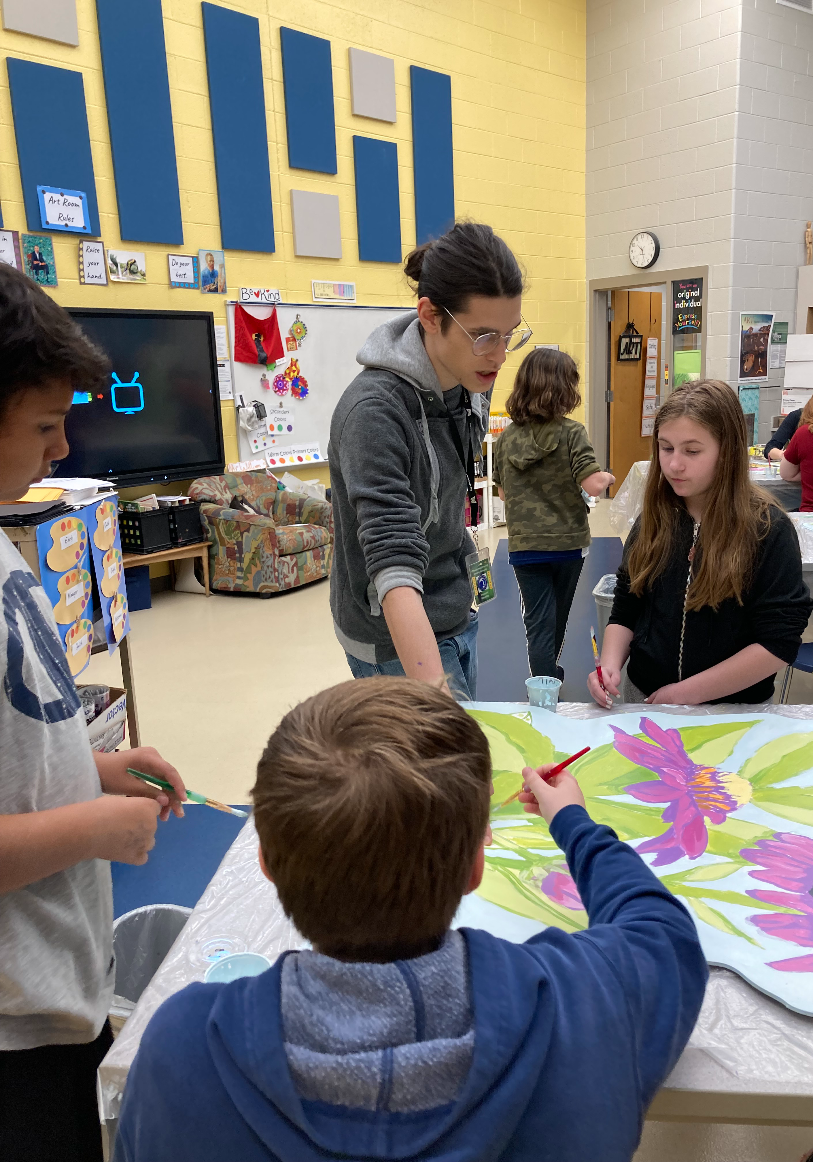 Students in art room. Teacher assisting them.