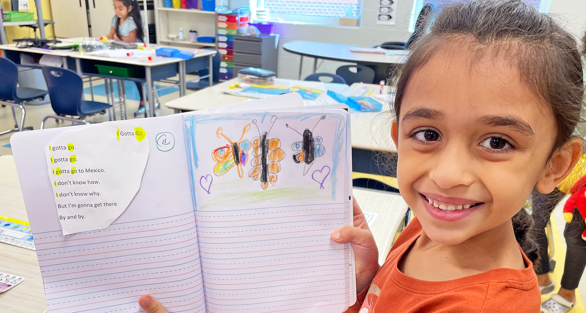 child holding up her notebook showing the story she made.