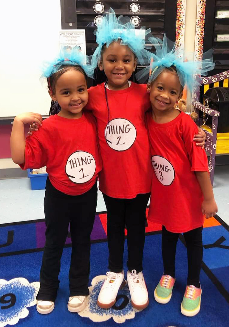 Three girls do a hug pose dressed as Thing One, Thing Two and Thing Three.