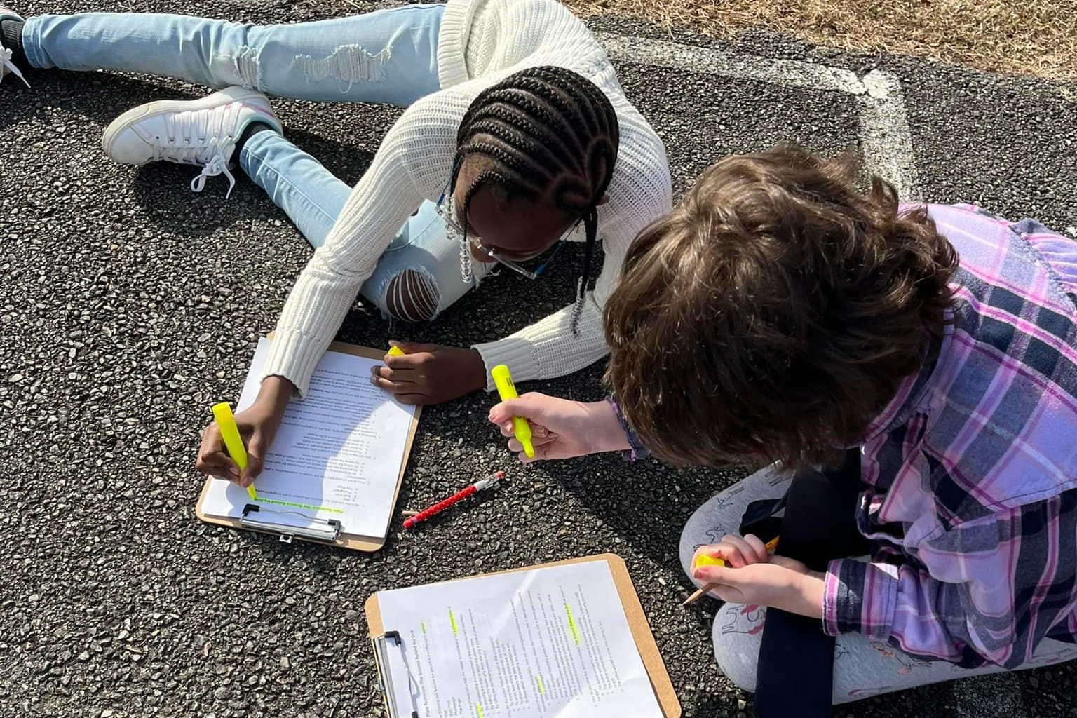 Two students outside on ground working together on a project.