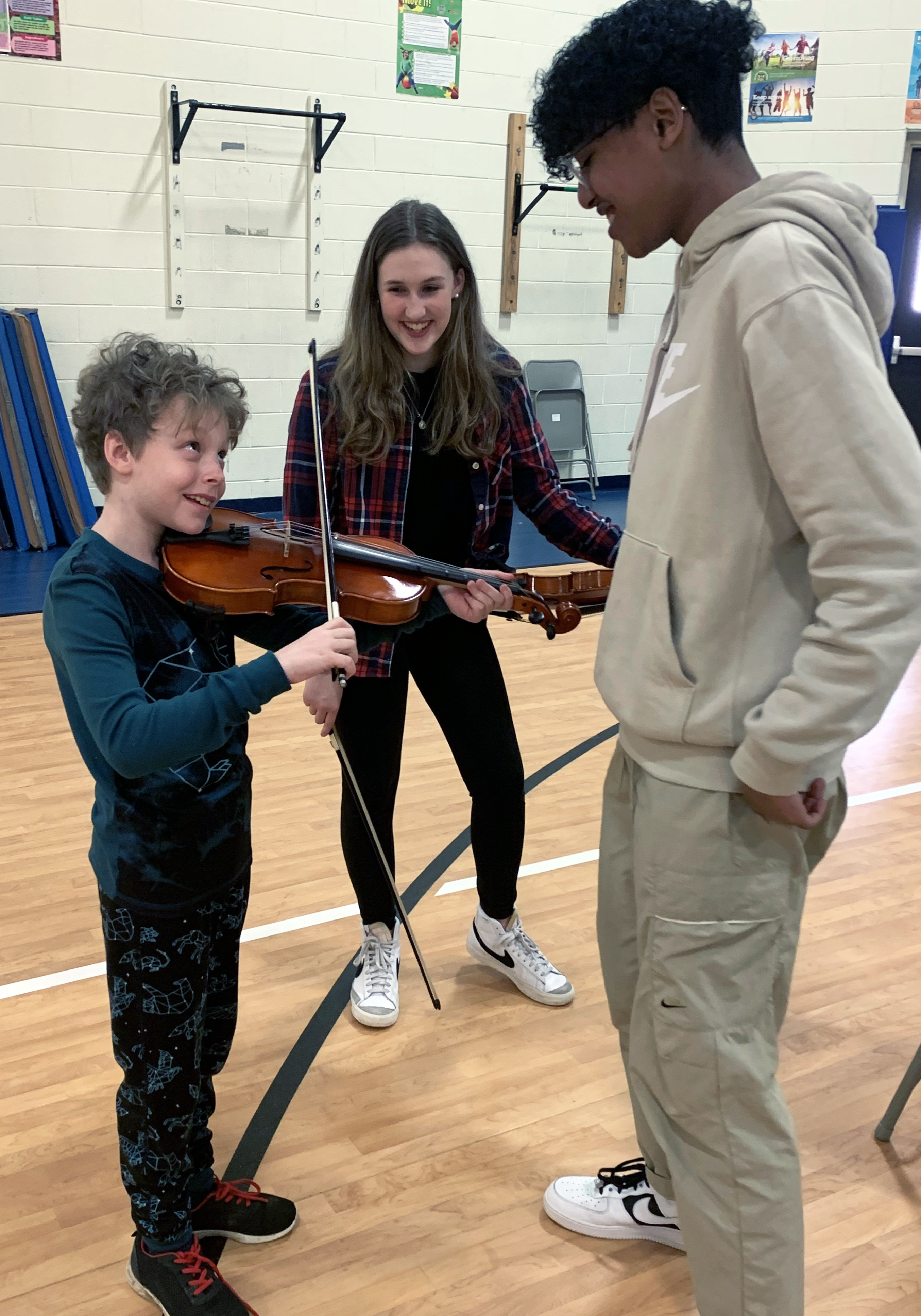 Young boy learning violin with two instructors helpiing.