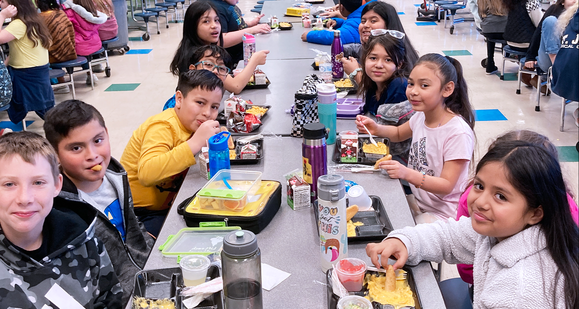 students sitting at the lunch table with food in a lunchbox