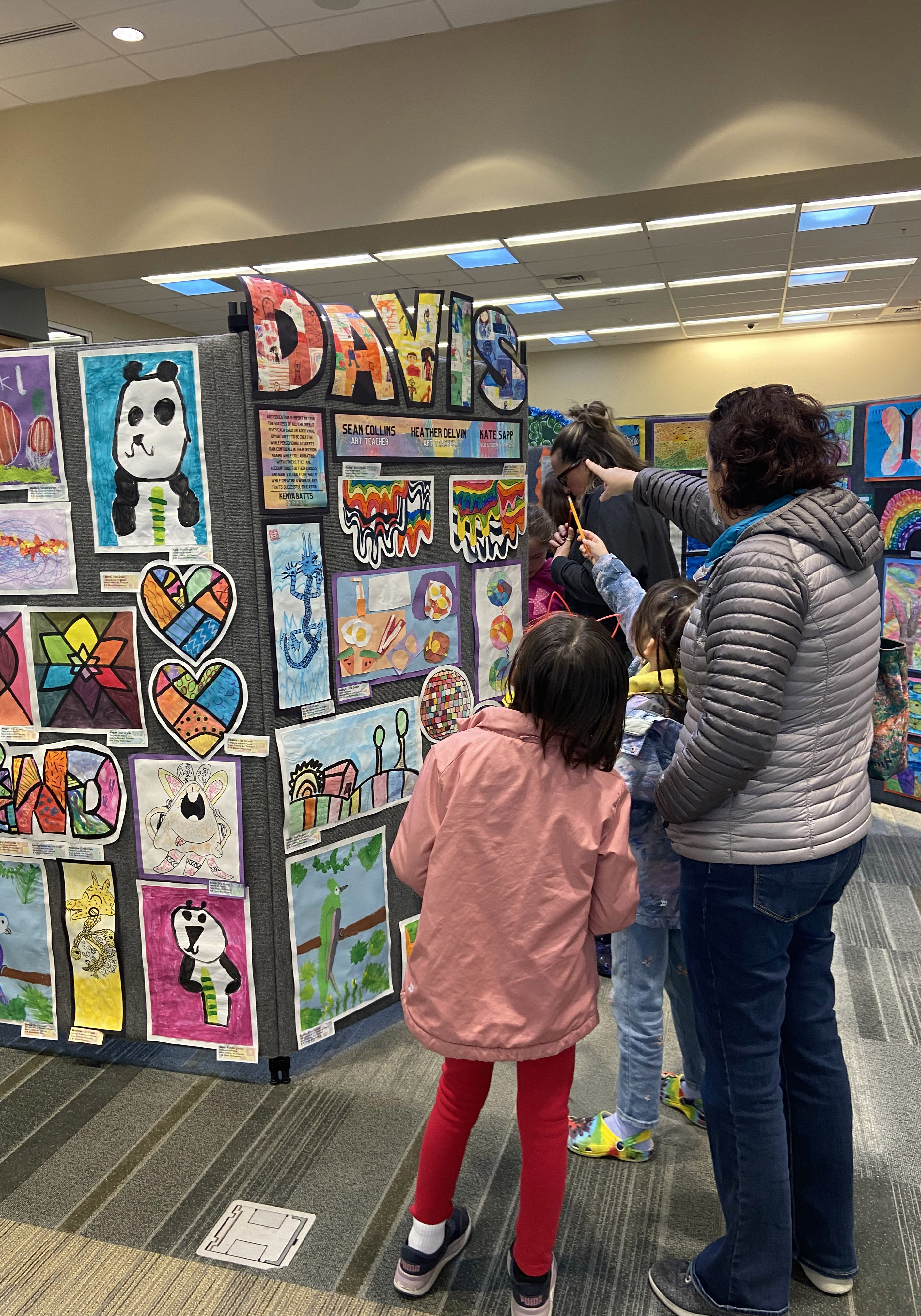 A woman and two girls observe artwork in the library