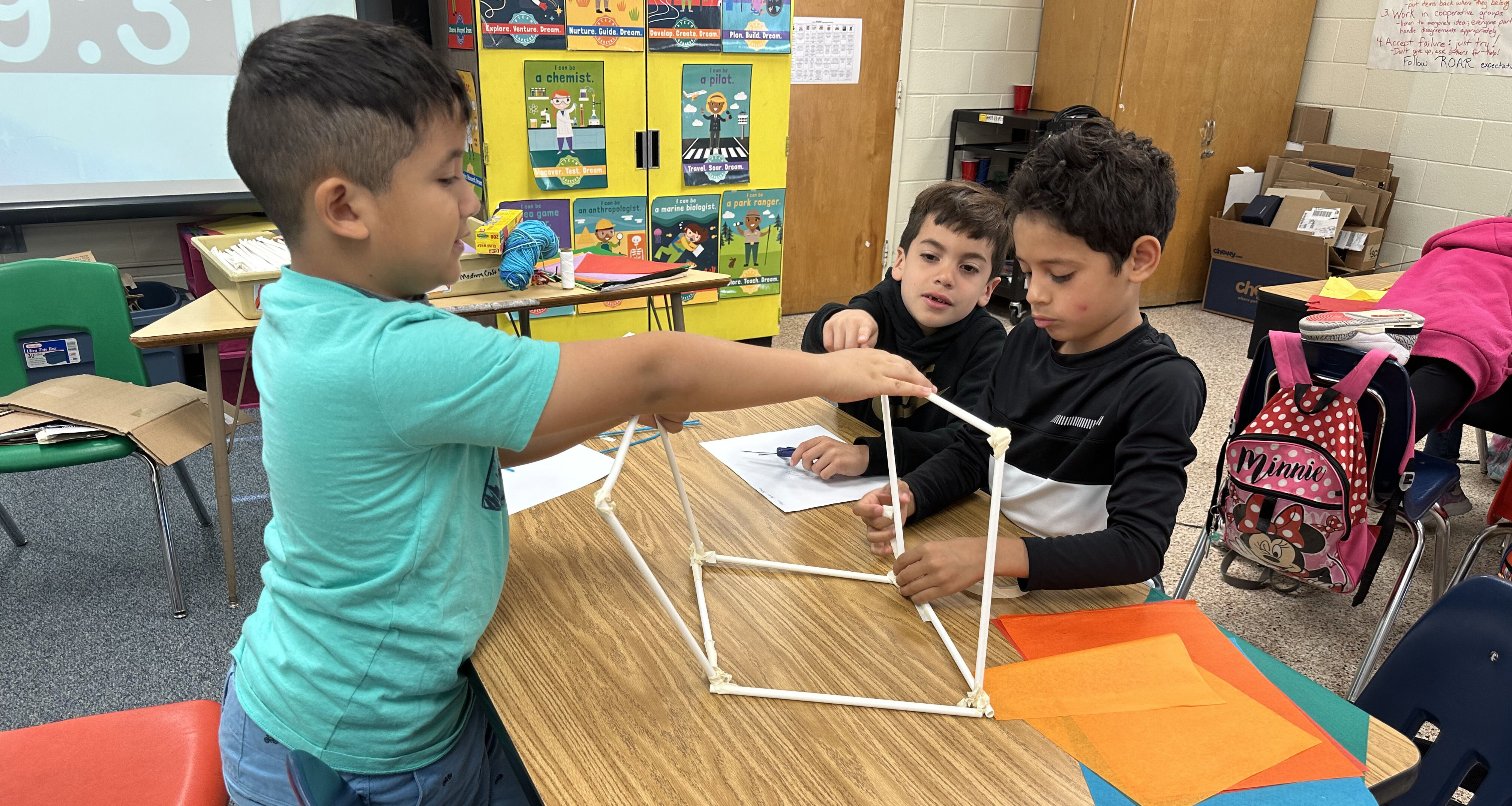 Three students are working on building a structure with straws
