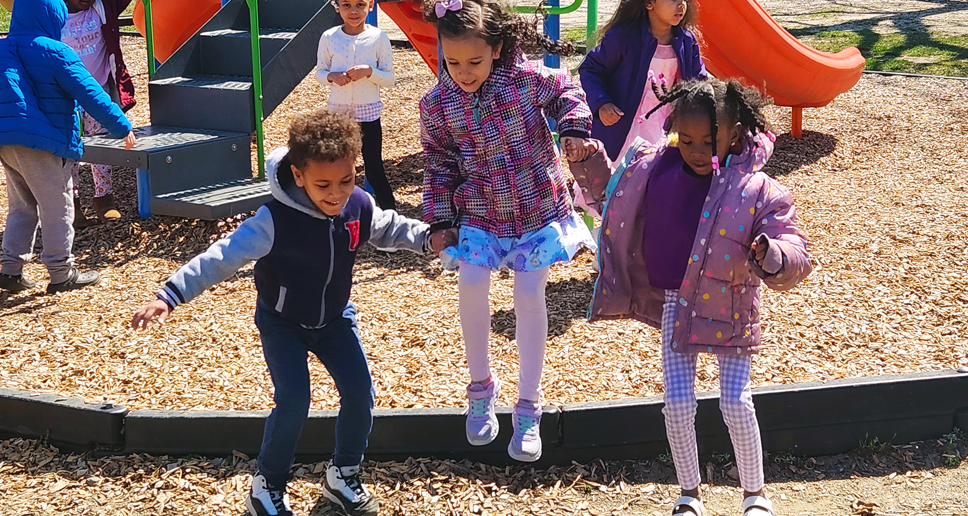 Three students hold hands and jump at playground