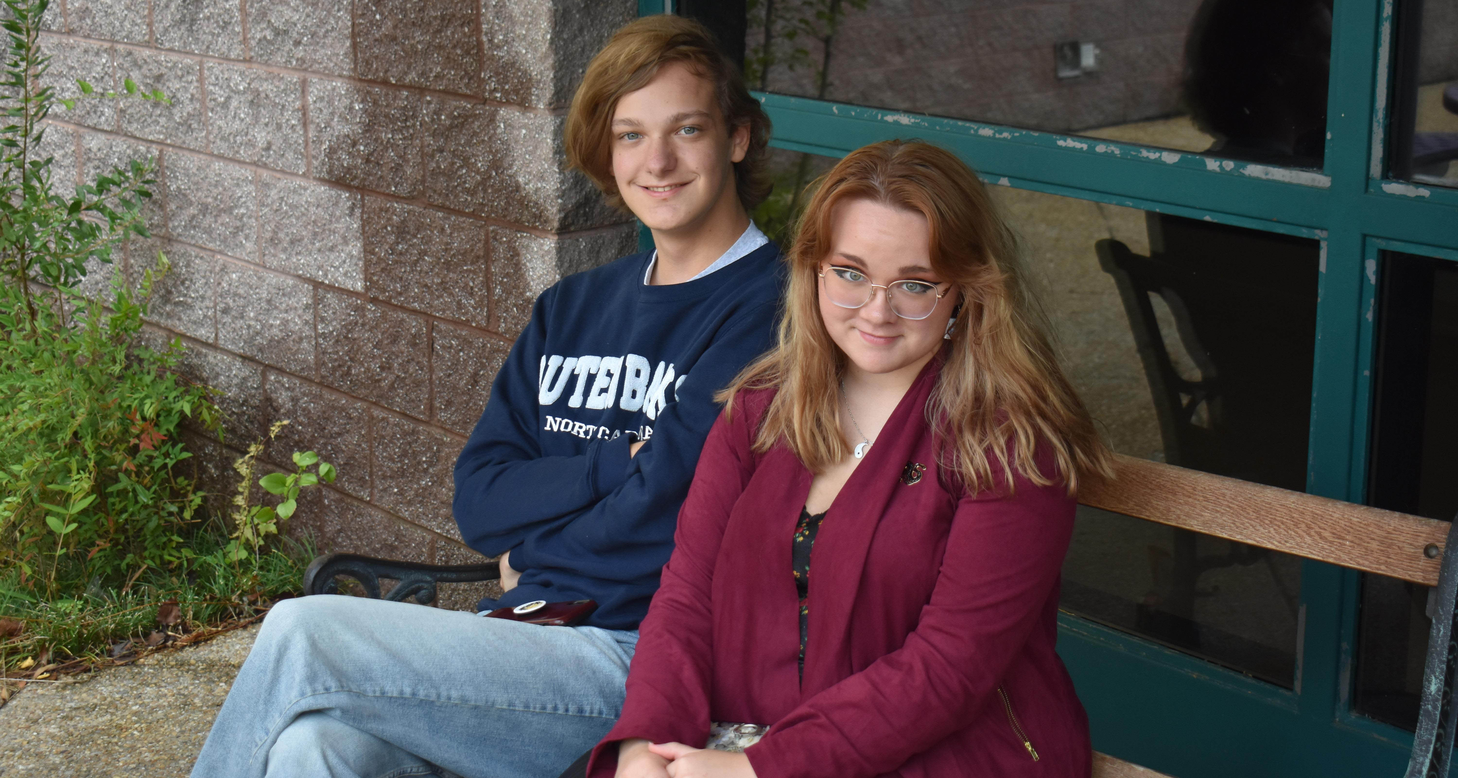 Two students sitting on a bench outside of the school building
