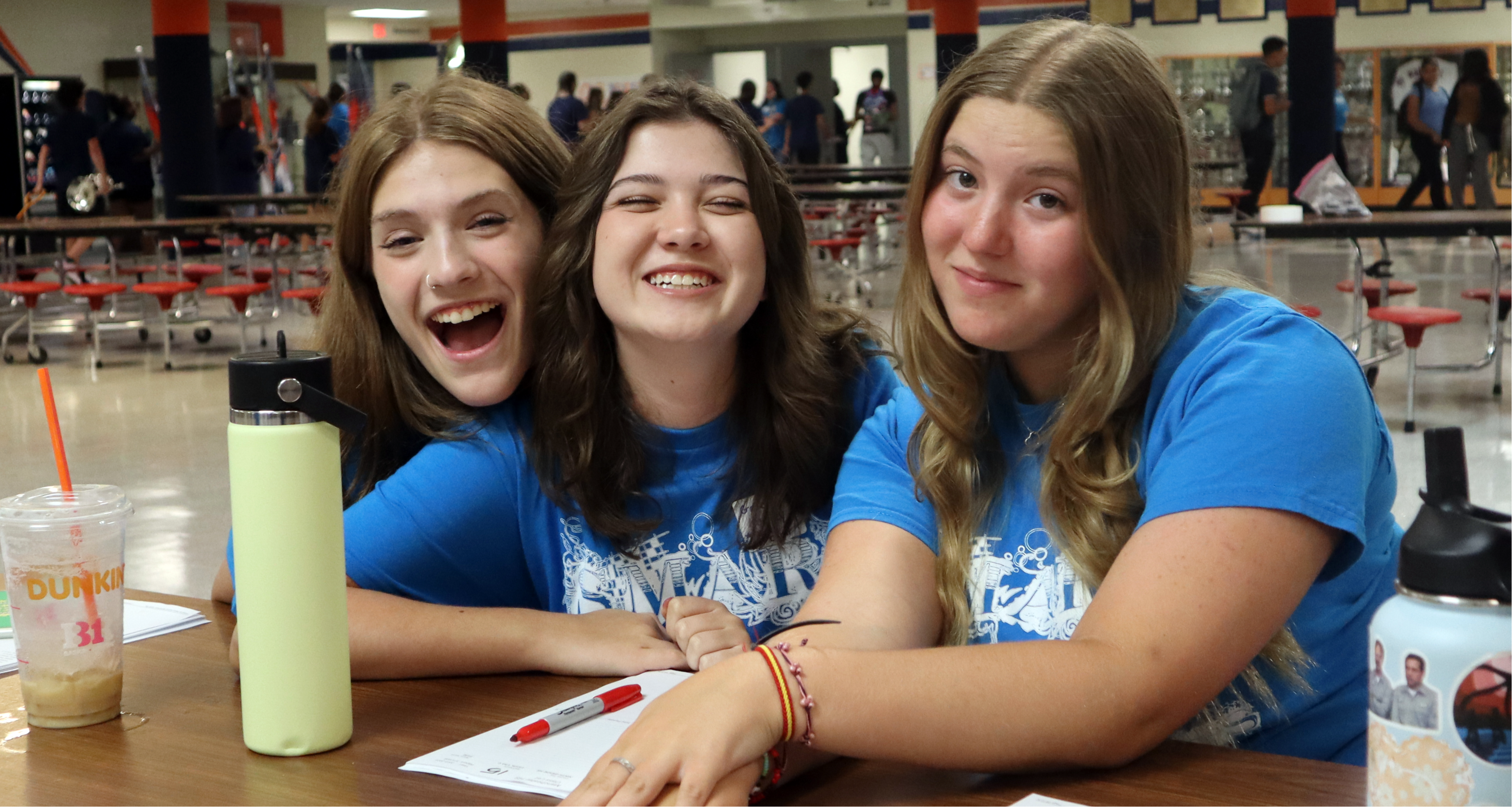 Three girls smiling while sitting in the school cafeteria