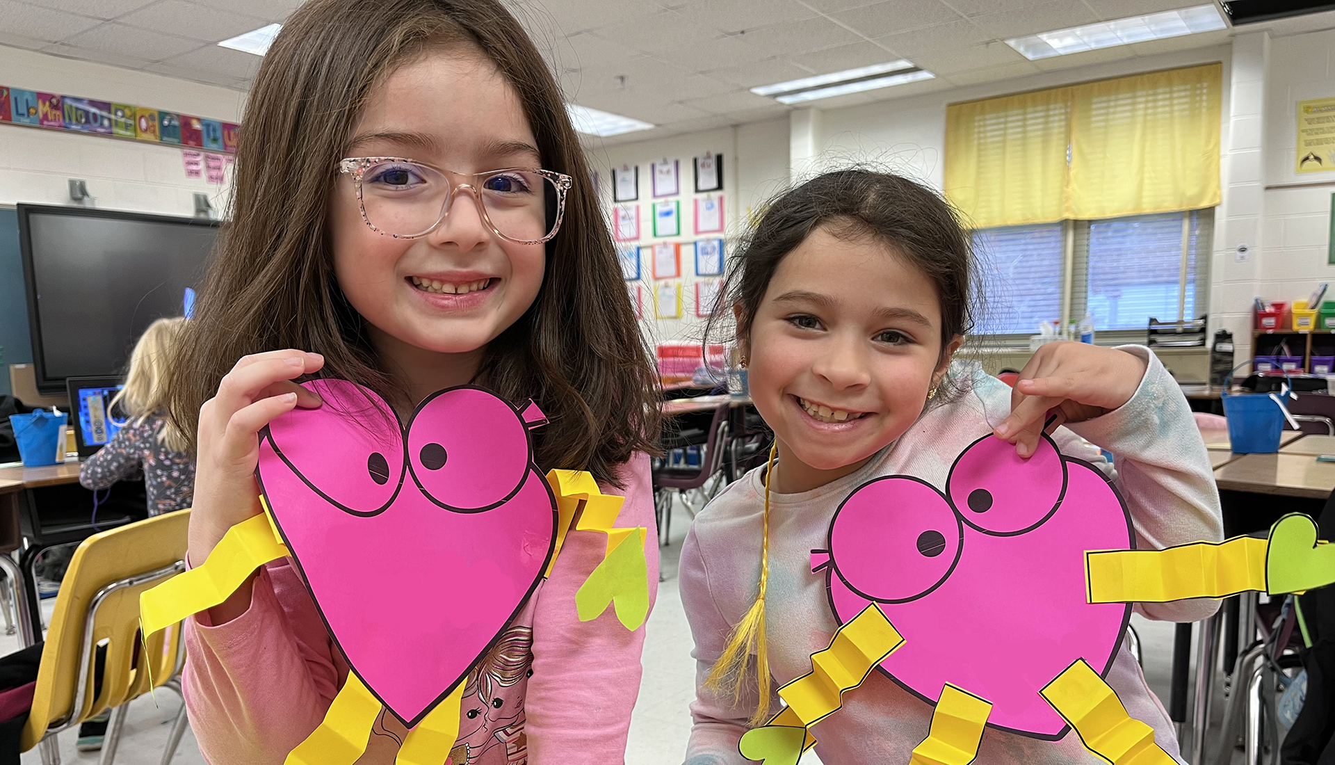 Two young girls holding up a heart shape project they made.