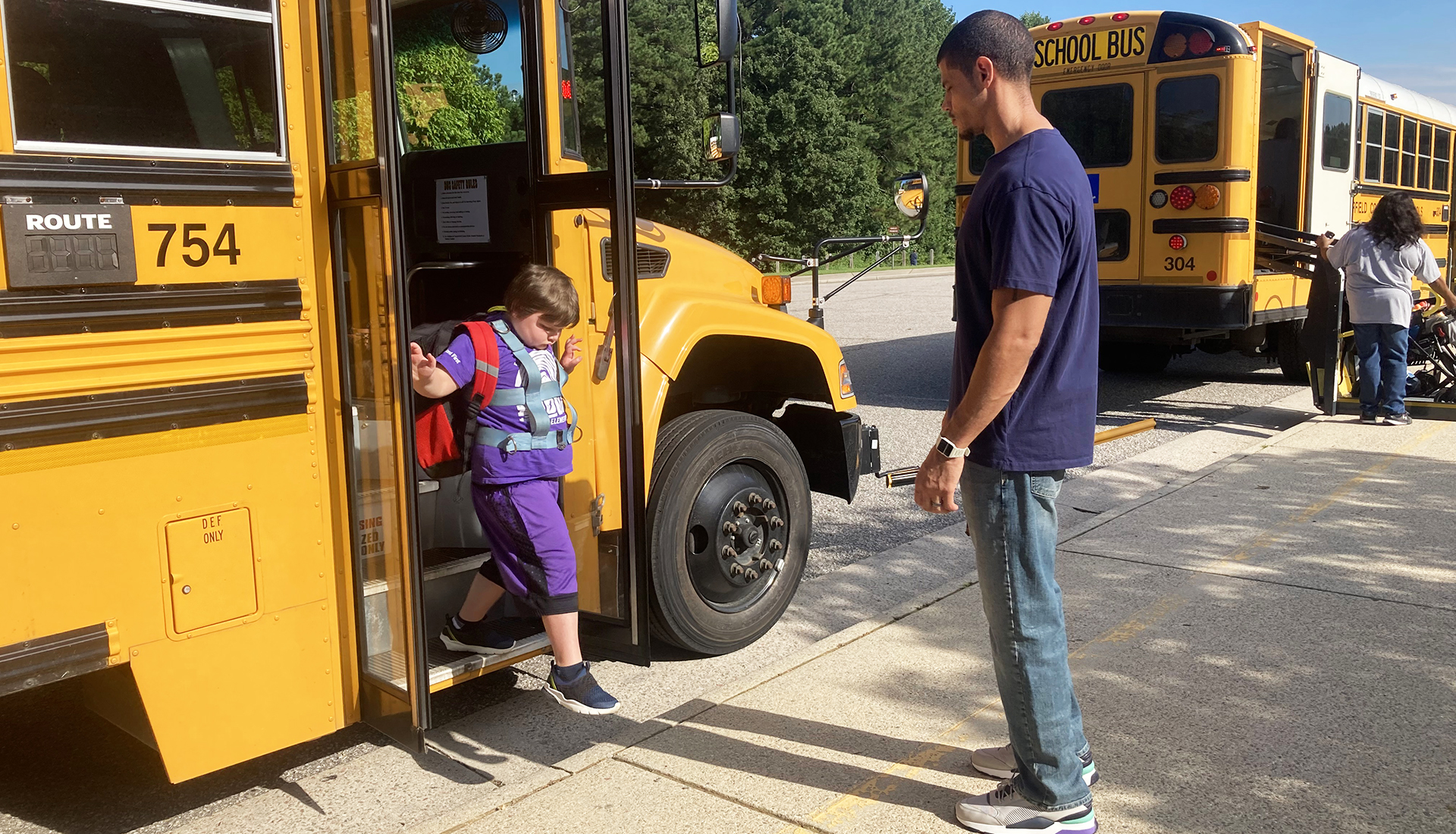 Student getting off a bus while teacher awaits.