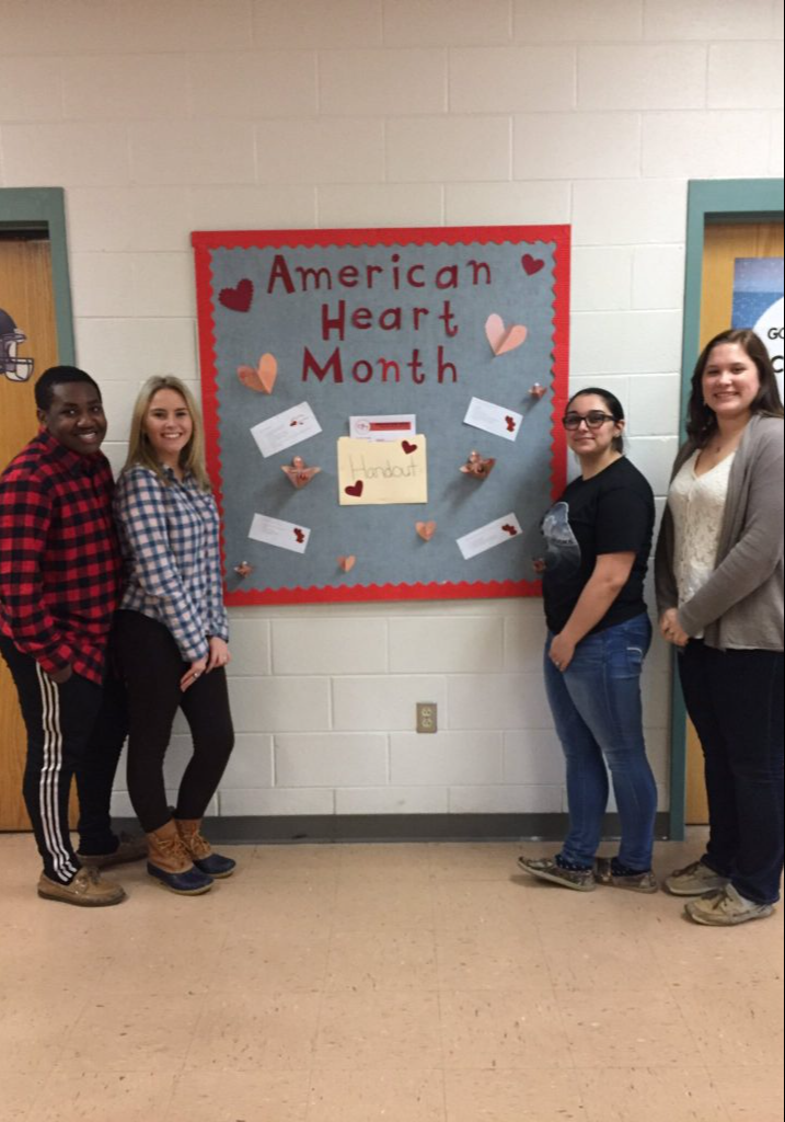 Four students pose for a photo near an American Heart Month sign