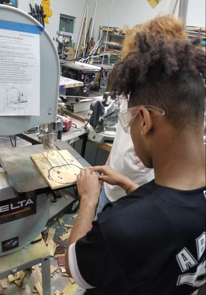 A student cutting a piece of wood in class