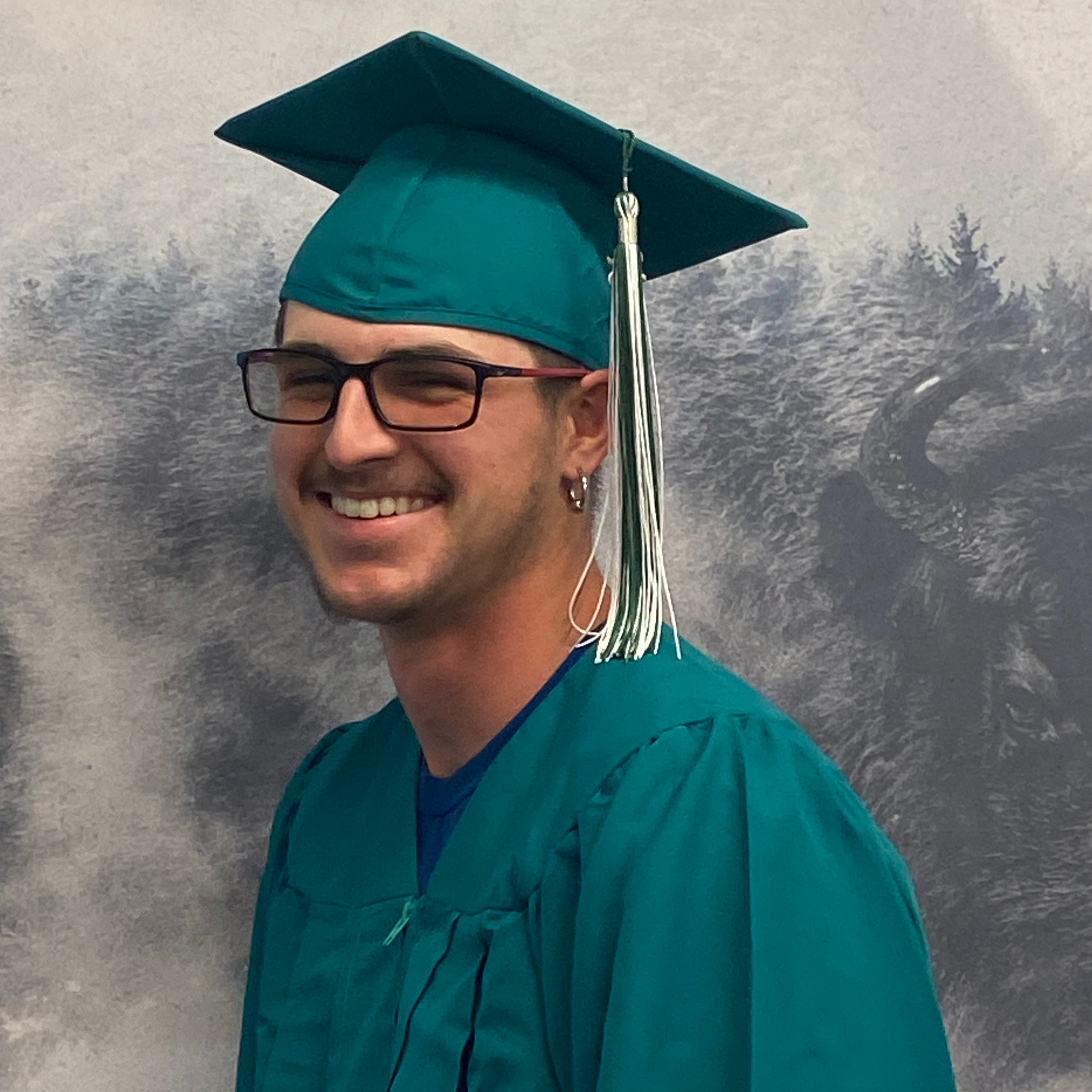 Trayden Pierce in green graduation robes and cap
