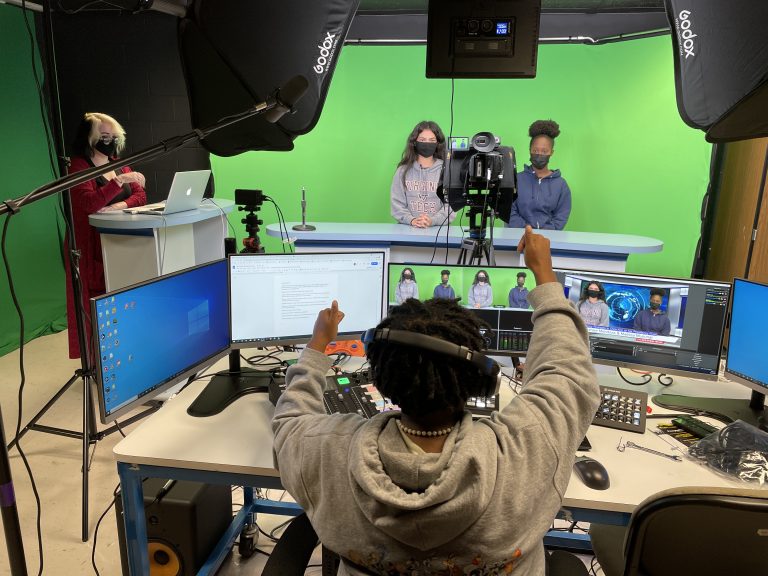 A student filming two other students on a green screen