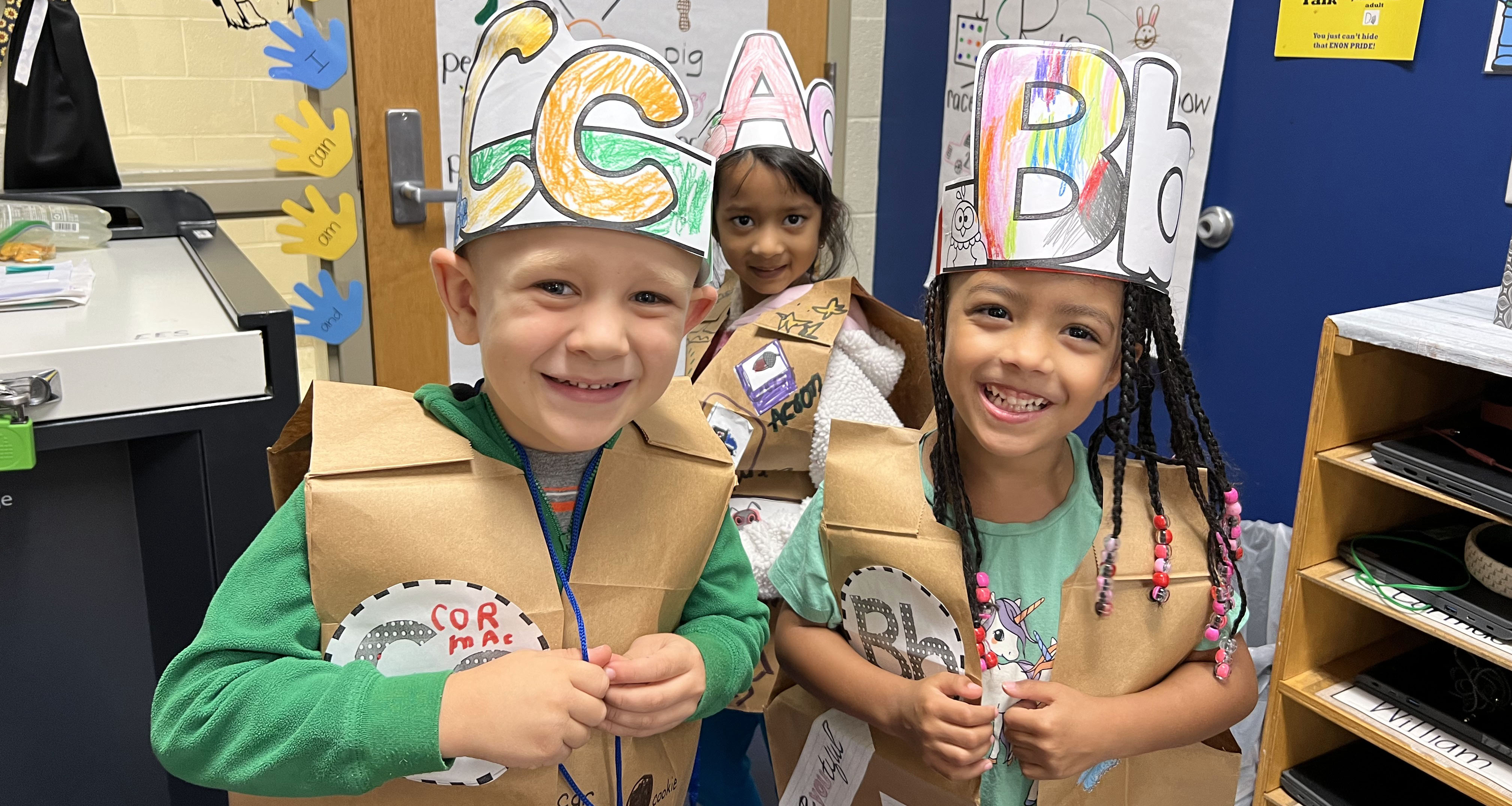 Three kindergartners wearing costumes made out of paper