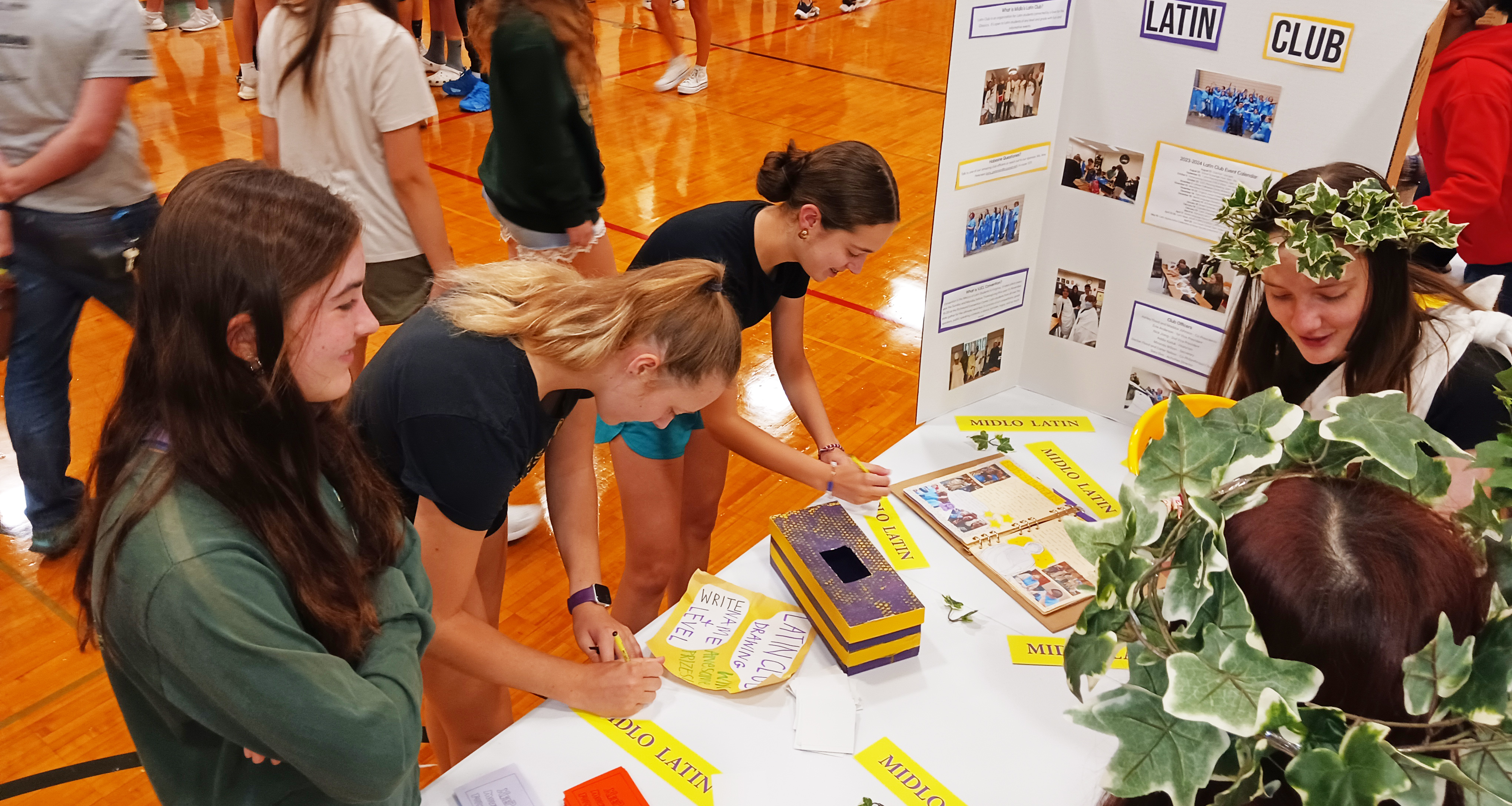 Students visiting a table about the Latin Club in the school gymnasium