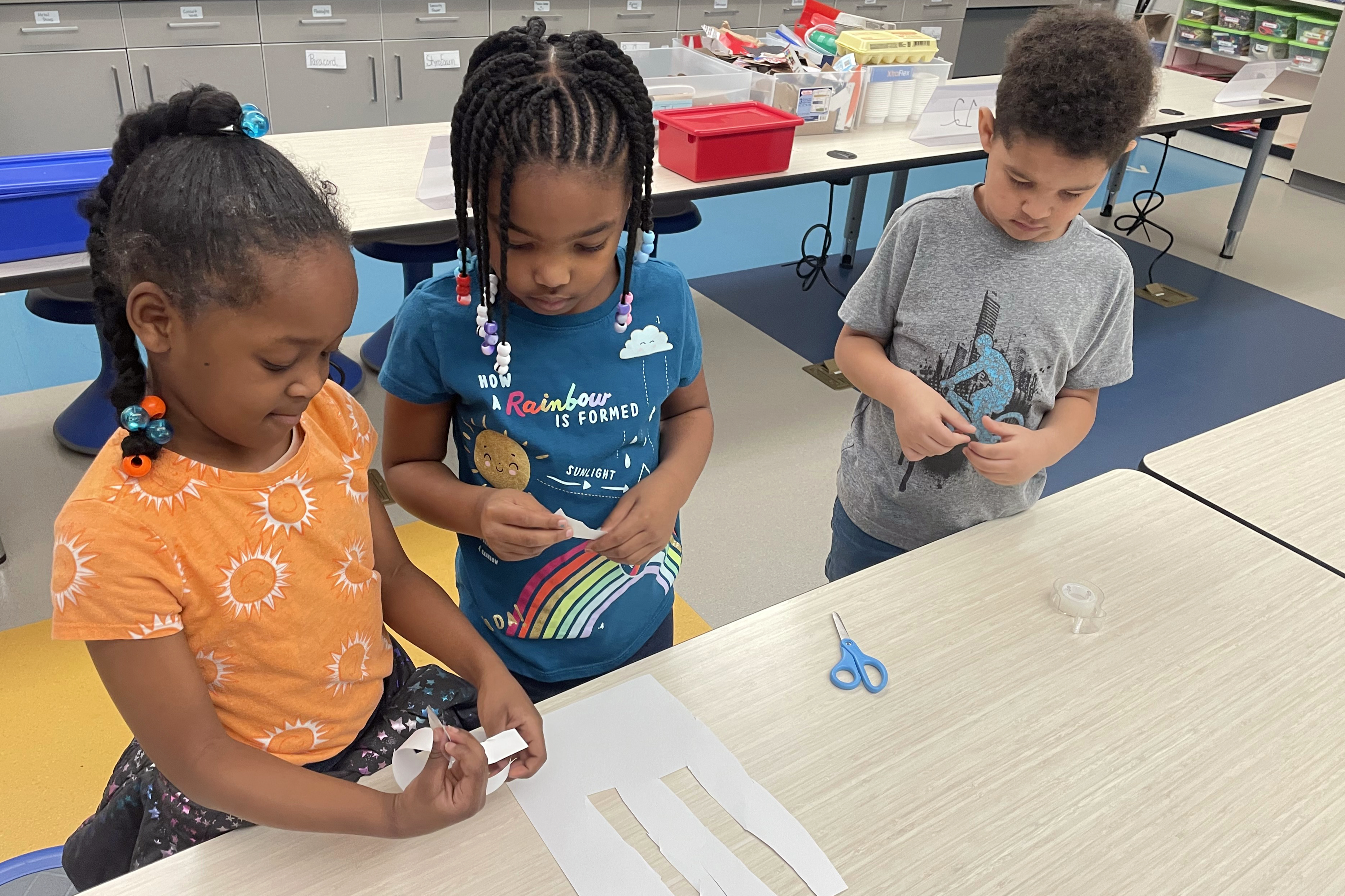 Three students cutting and taping paper