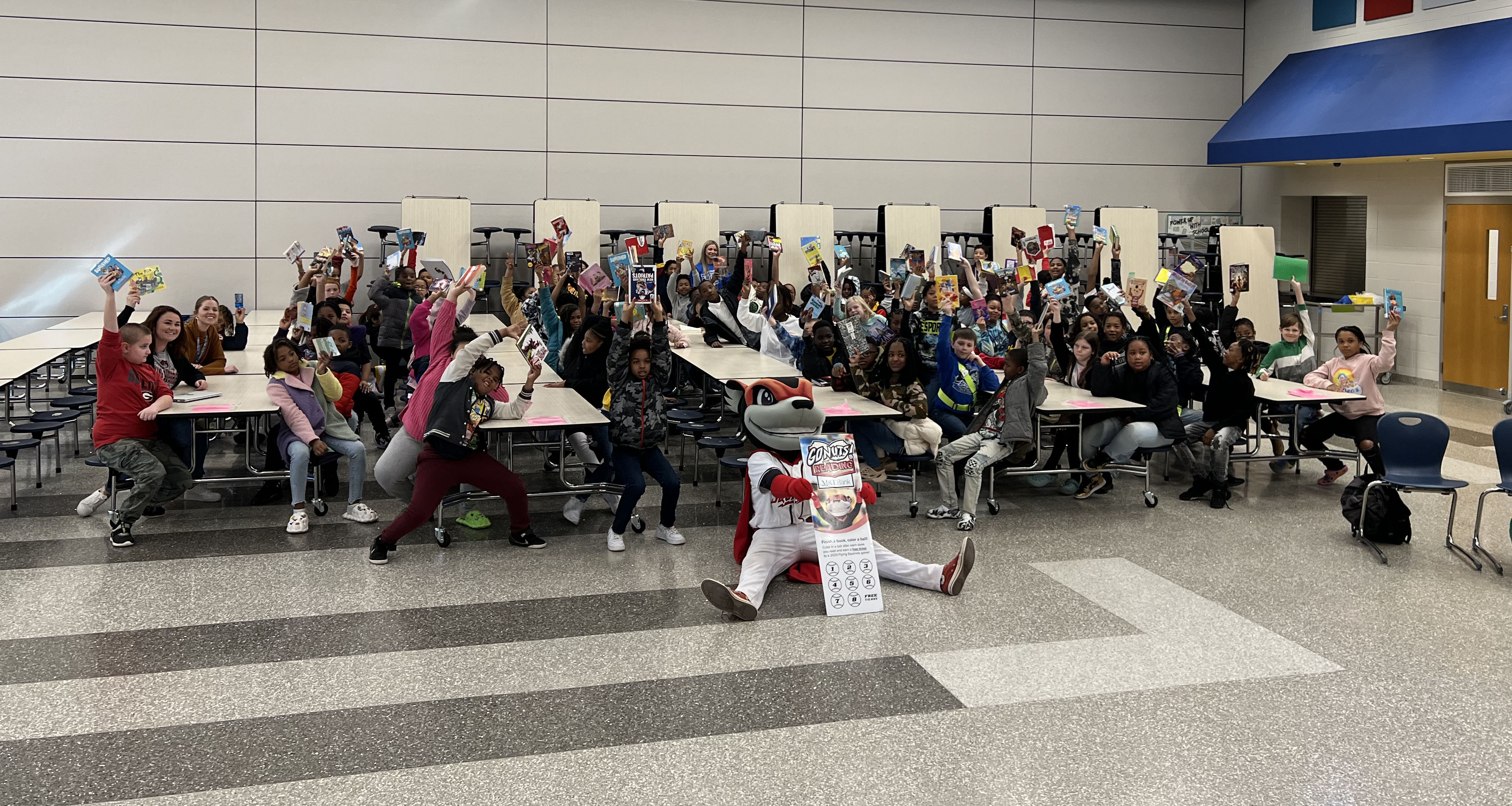 A large group of students holding up books in the cafeteria