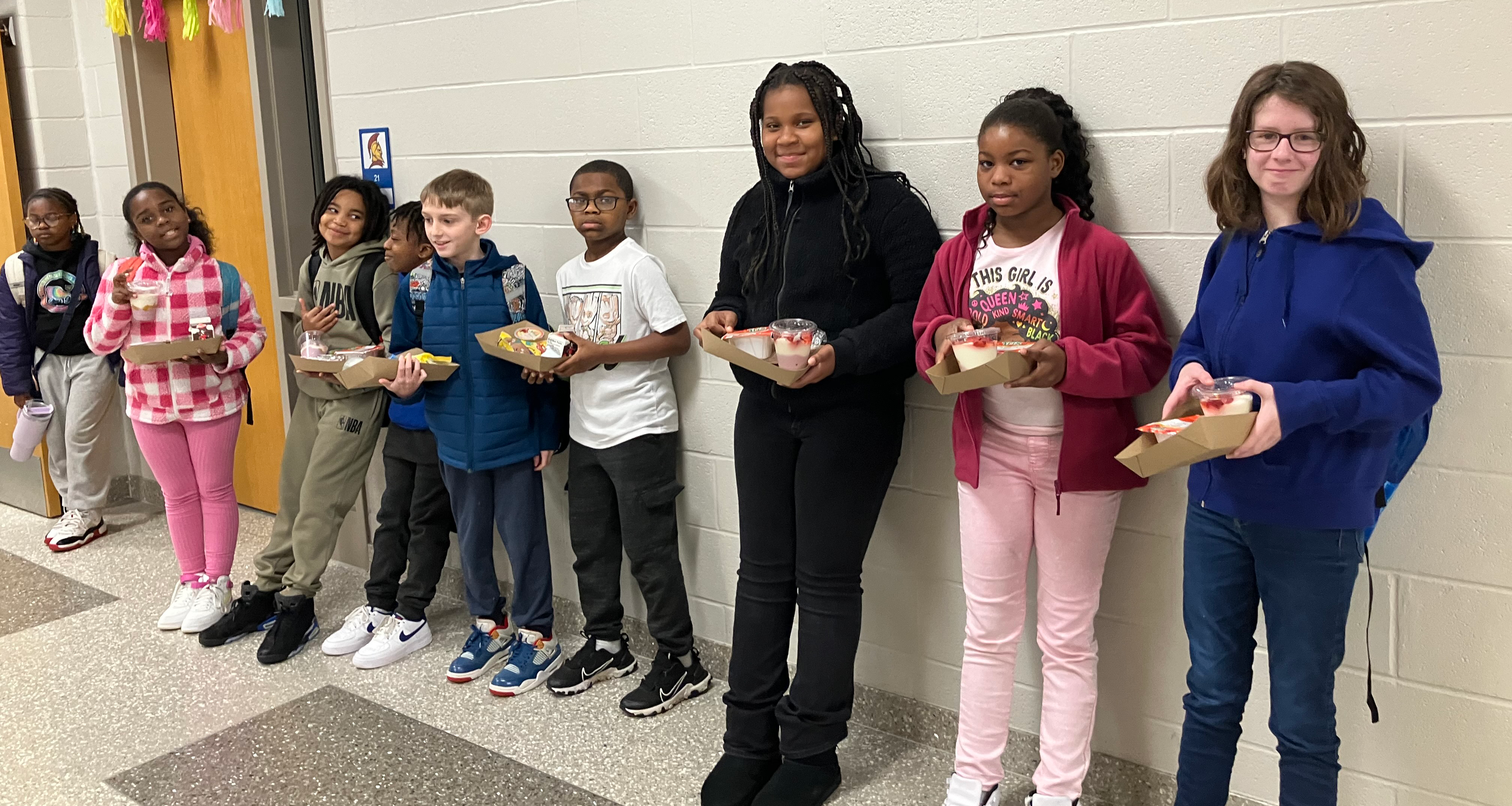 A group of students holding their lunches while standing in the hallway