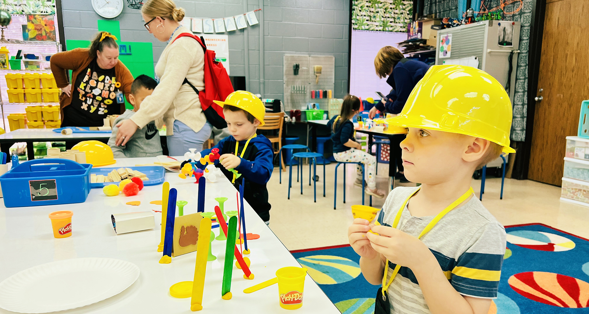 Young students building with blocks while wearing hardhats.