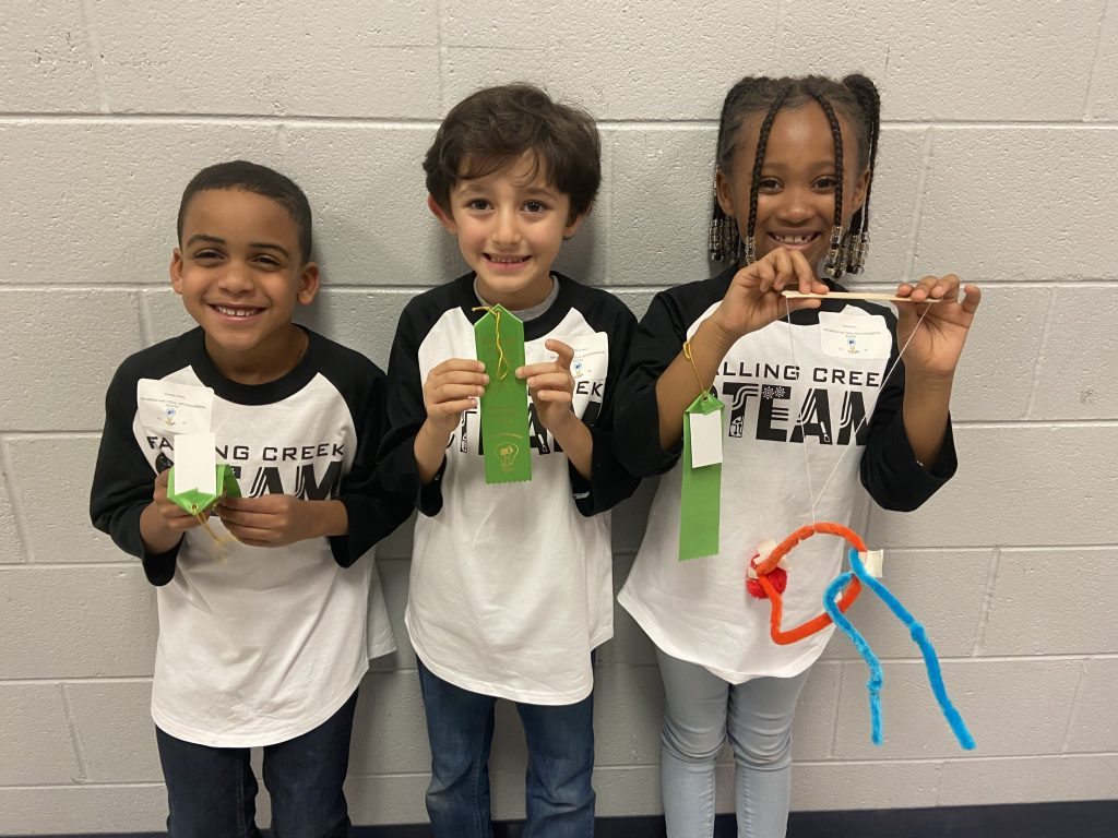 Three students holding up a ribbon that they won