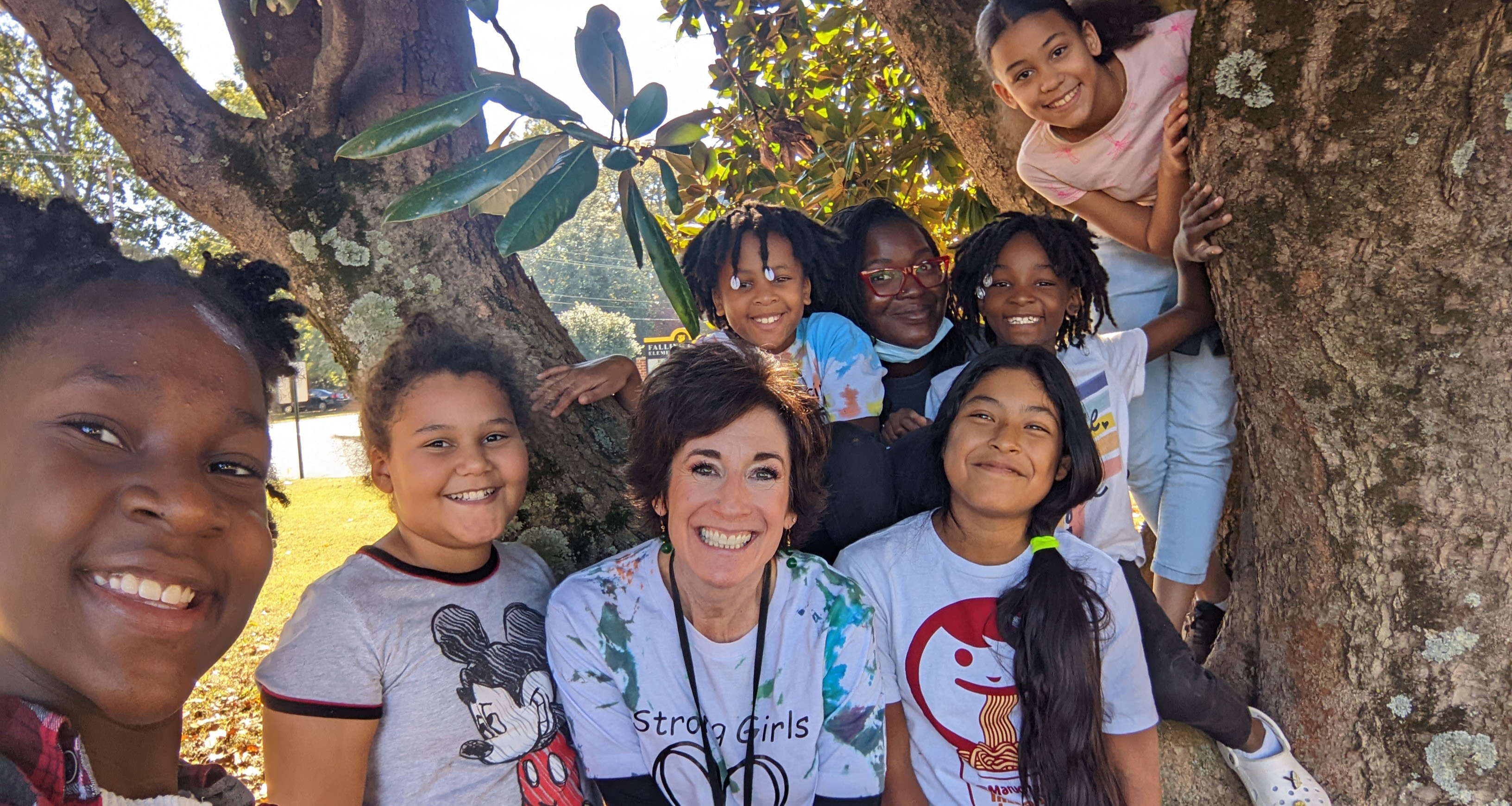 An administrator smiling with children in front of a tree