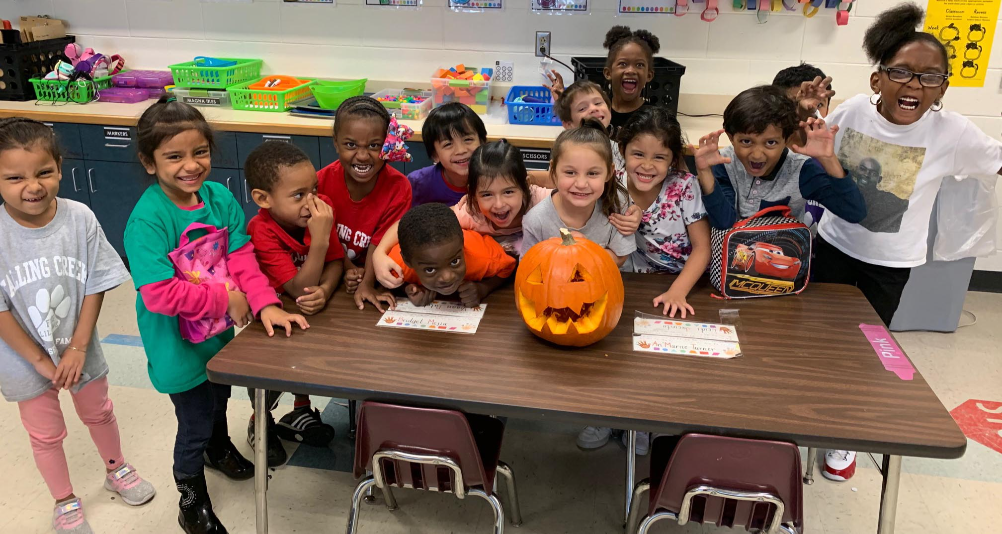A group of kindergartners pose in front of a pumpkin