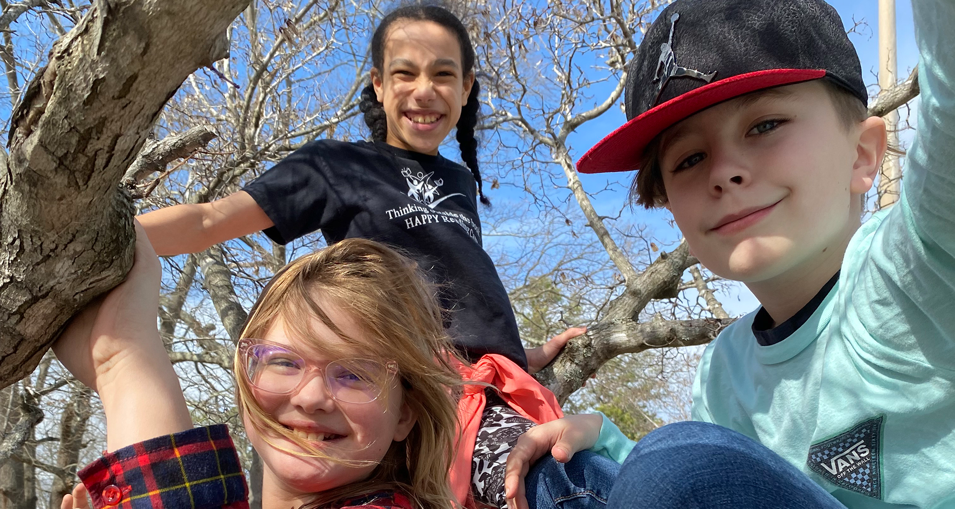 Three students in a tree smiling for the camera.