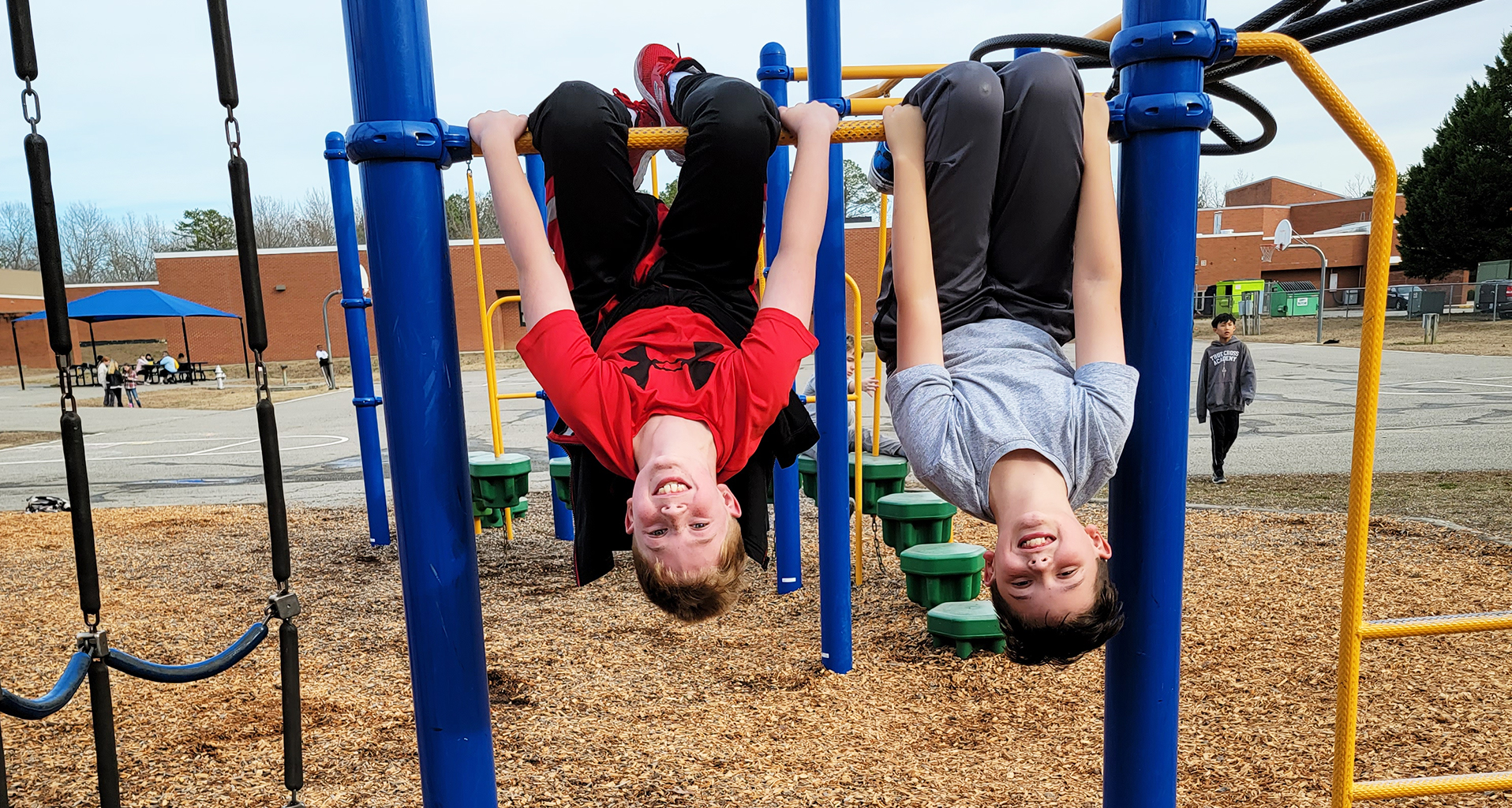 Two students hang upside-down on playground
