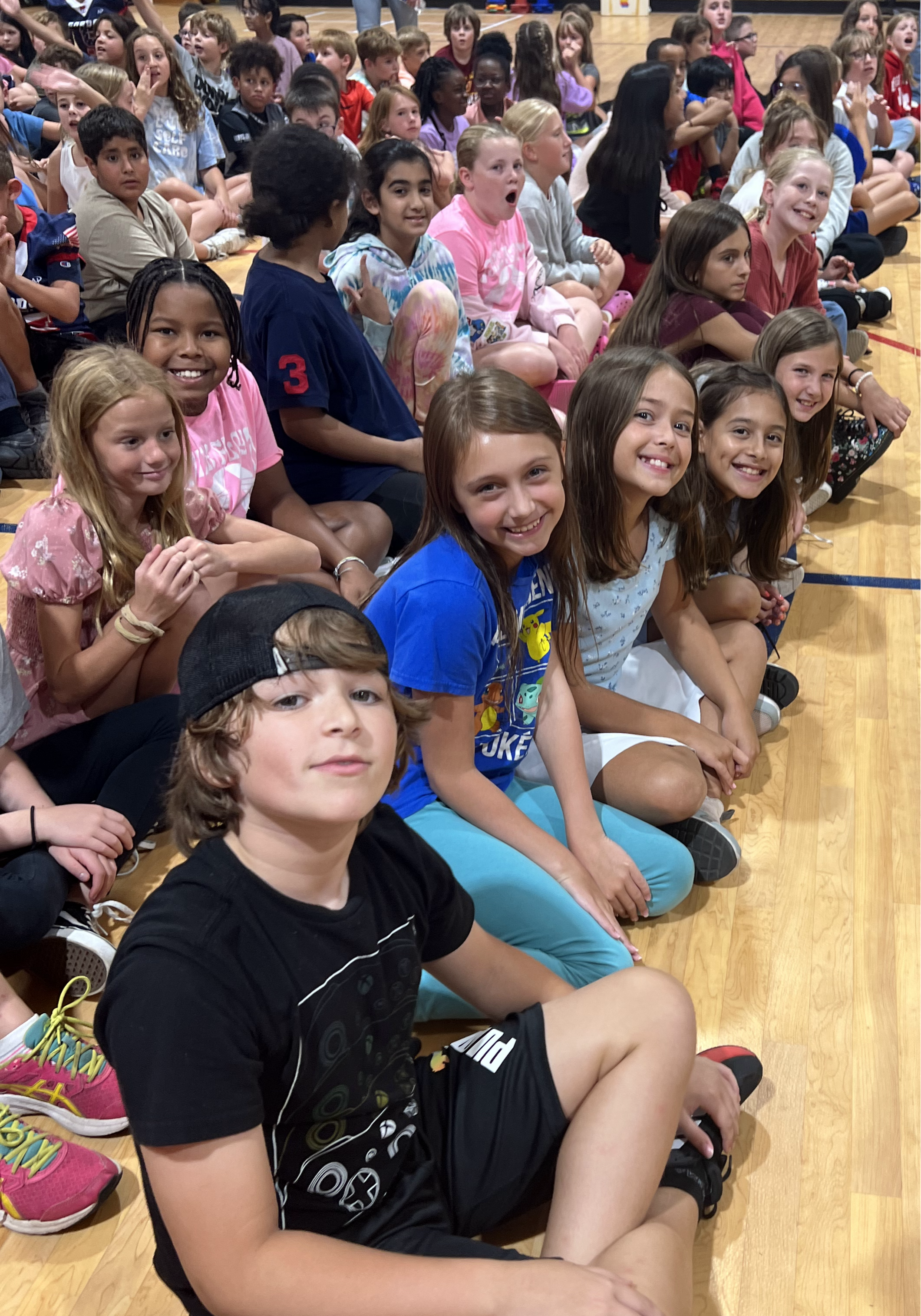 Students sitting on the floor in the gym for an assembly