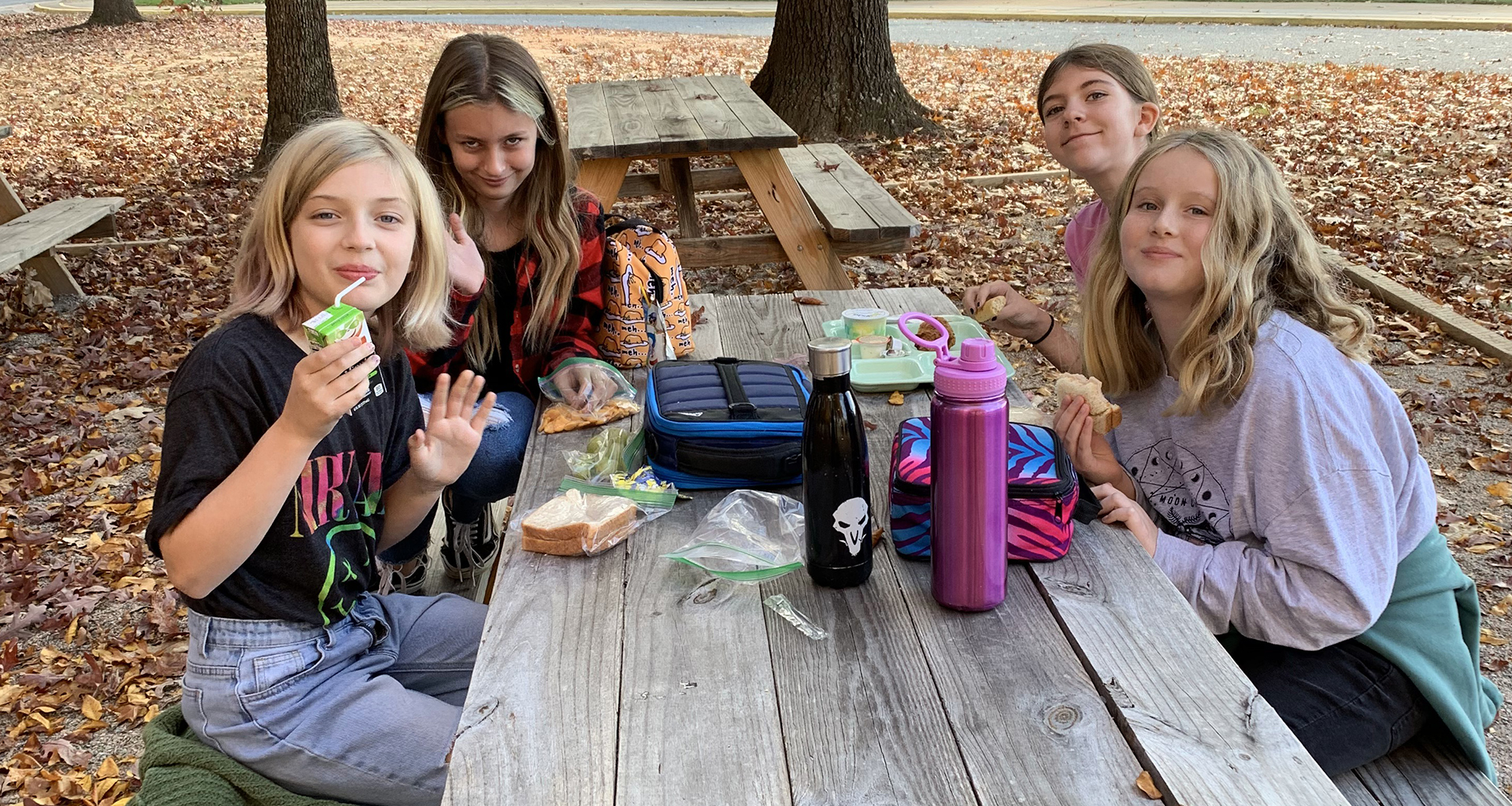 Four students eating outside on the picnic table.