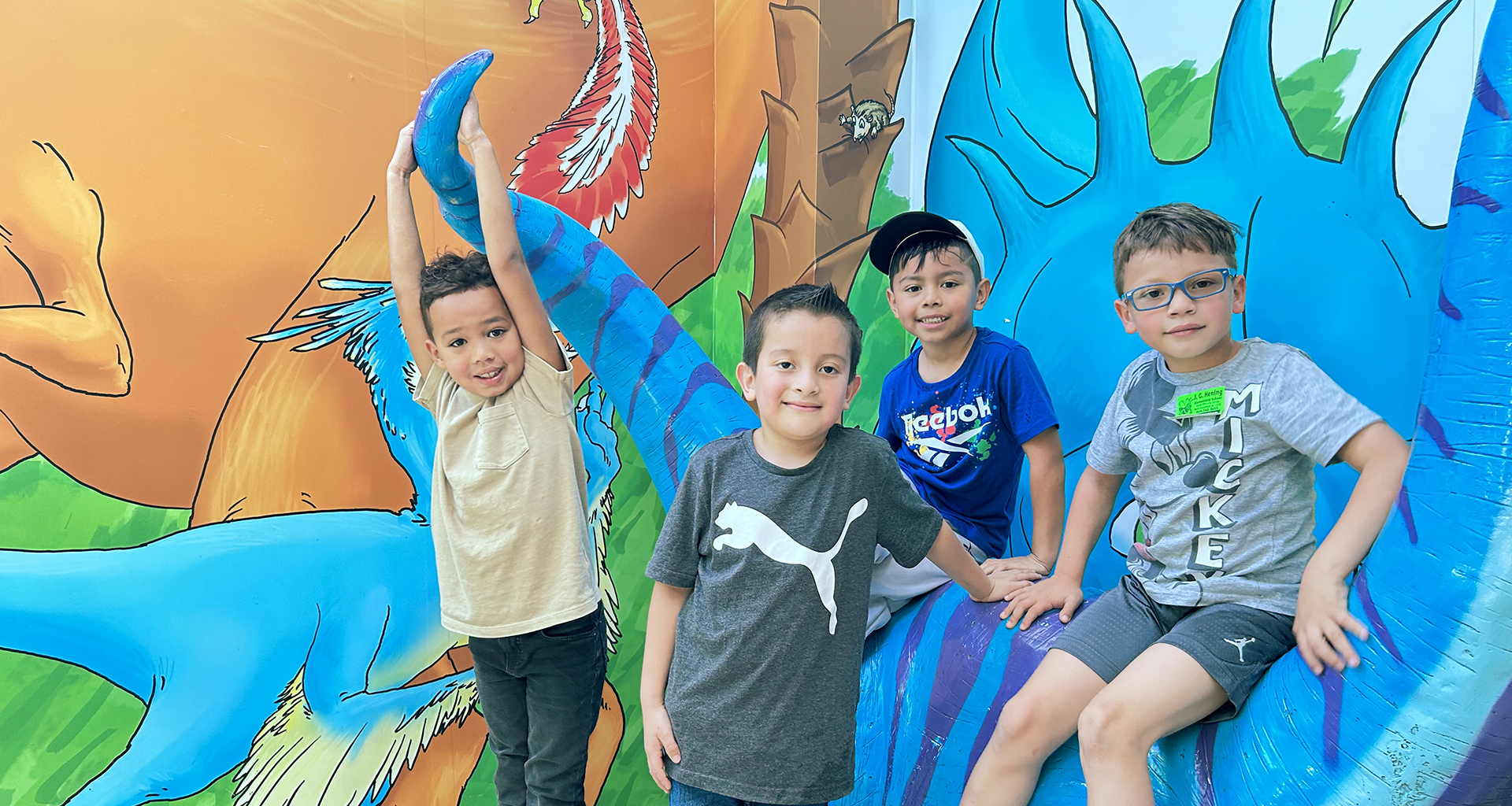 Four students pose in front of a mural.