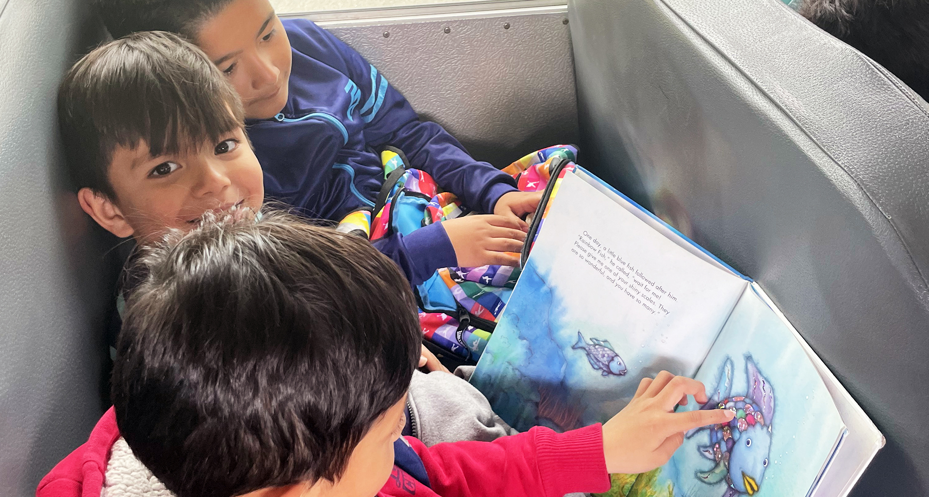 Three students reading a book on the bus.