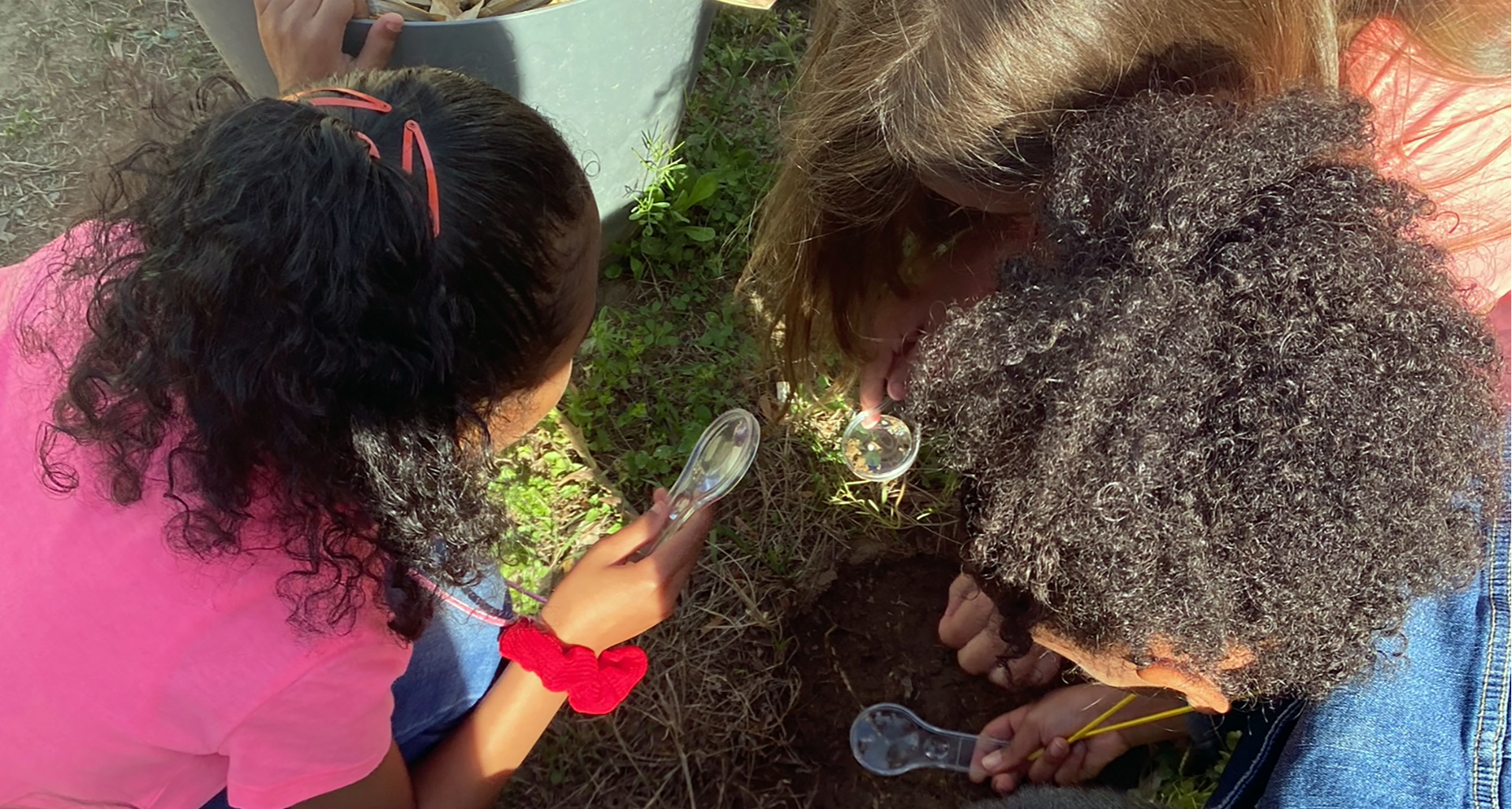 Three students examining the ground with magnifying glasses.