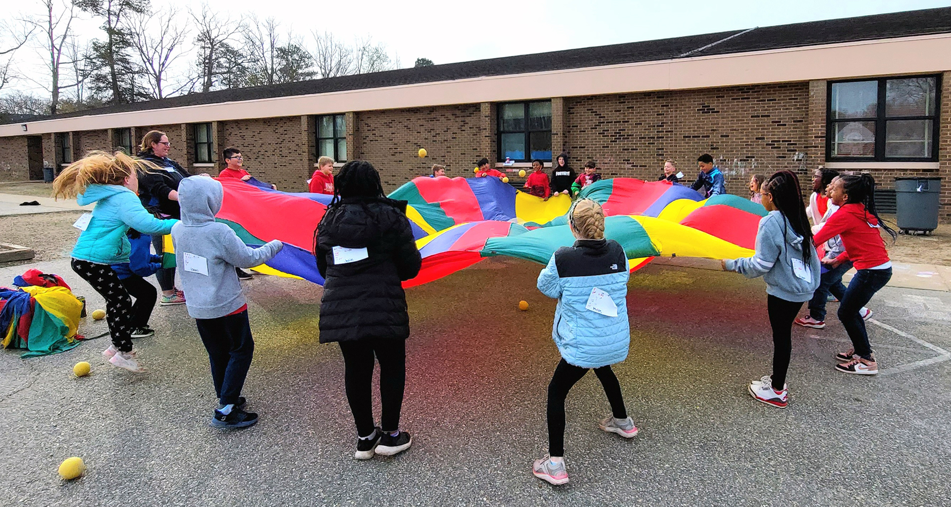 A group of students playing with a large colorful parachute and balls
