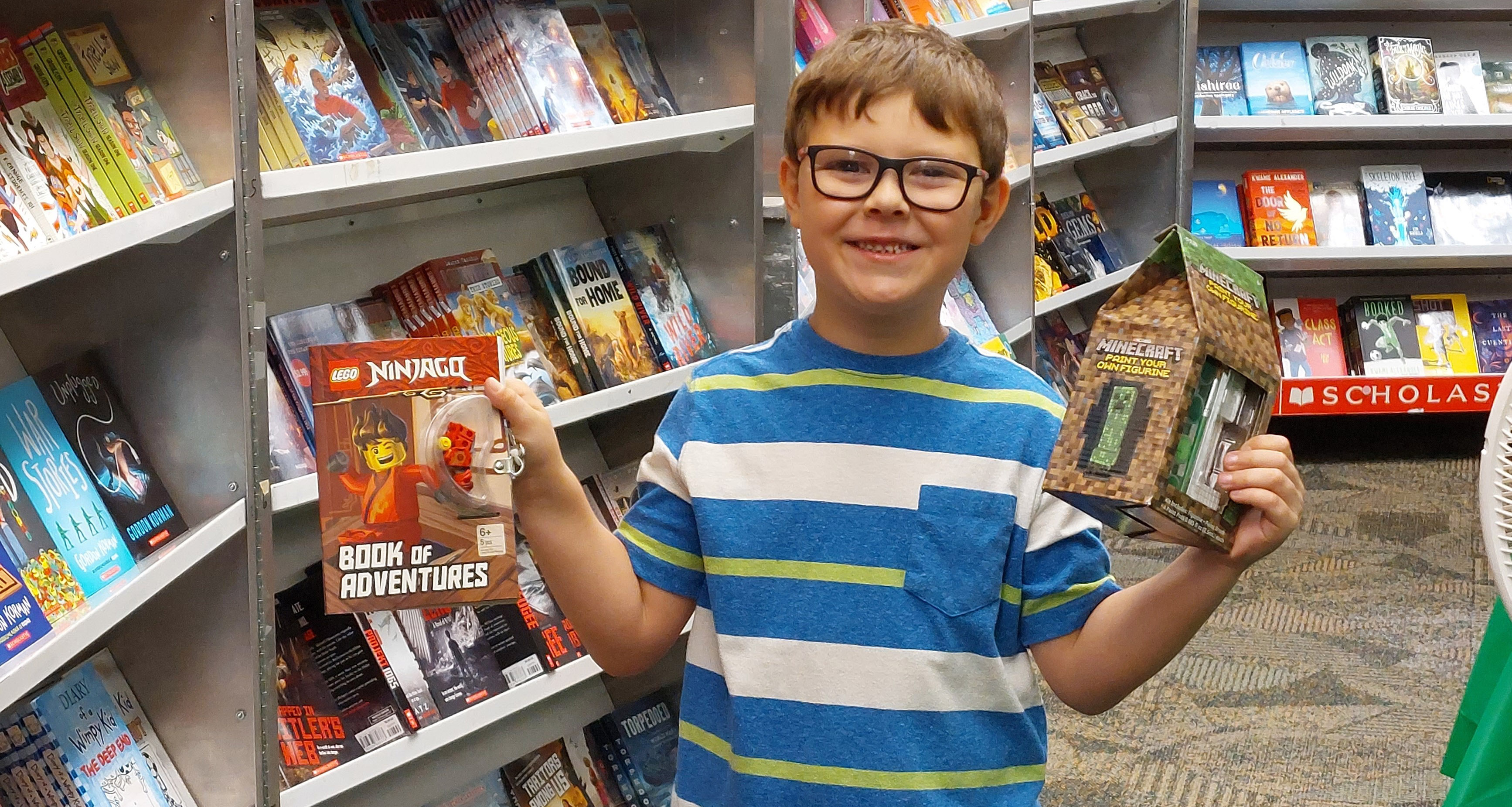 A boy holding up two books in the school library