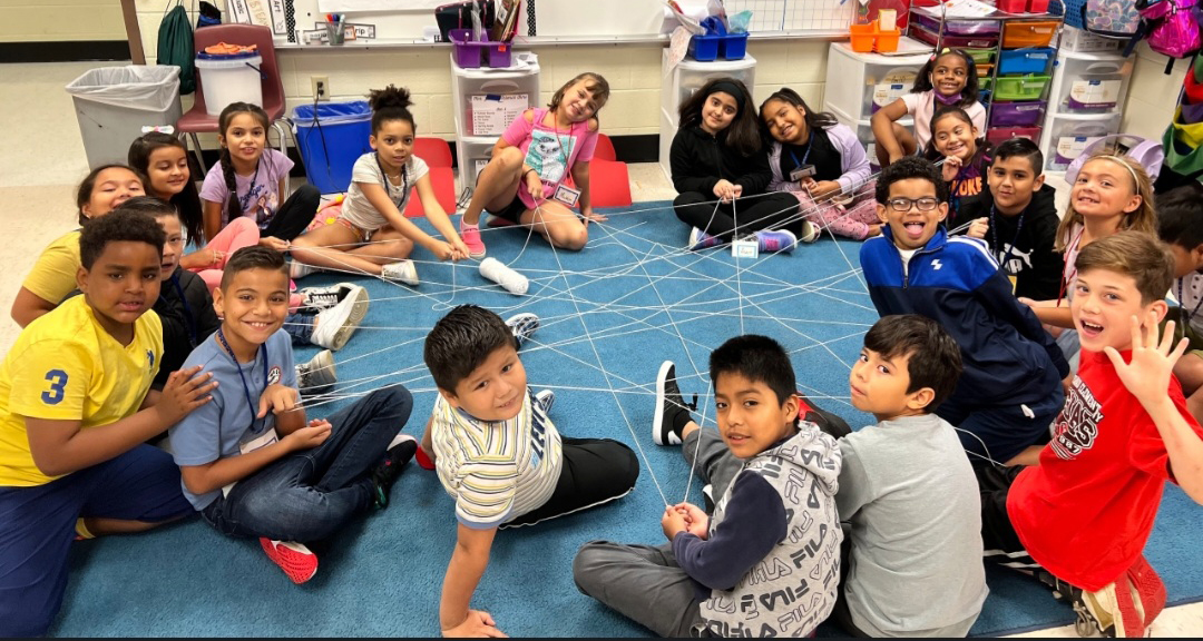 A large circle of students pulling on one long yarn string