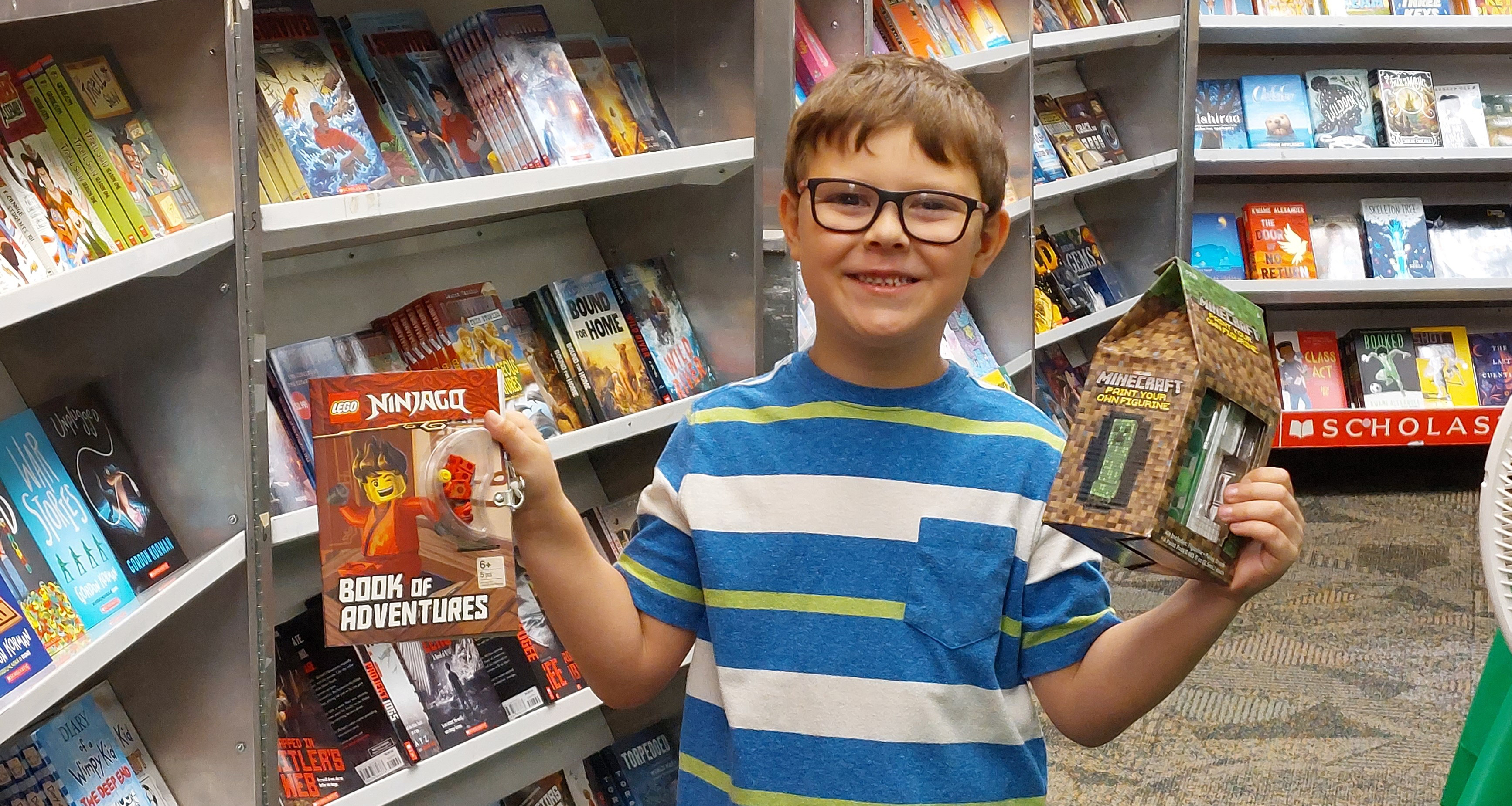 A boy holding up two book in the school library