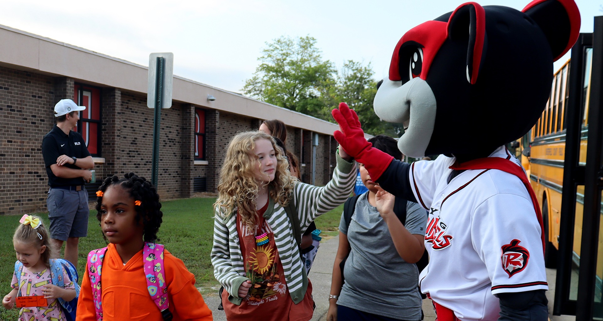 Students high five the mascot as they come off the bus